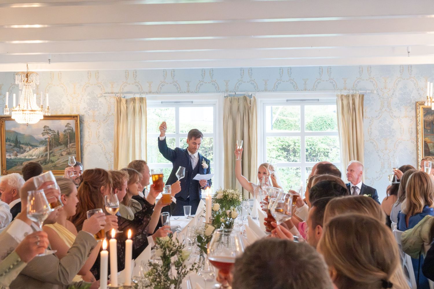 Groom raises a toast with wedding guests at an elegant candlelit reception dinner.