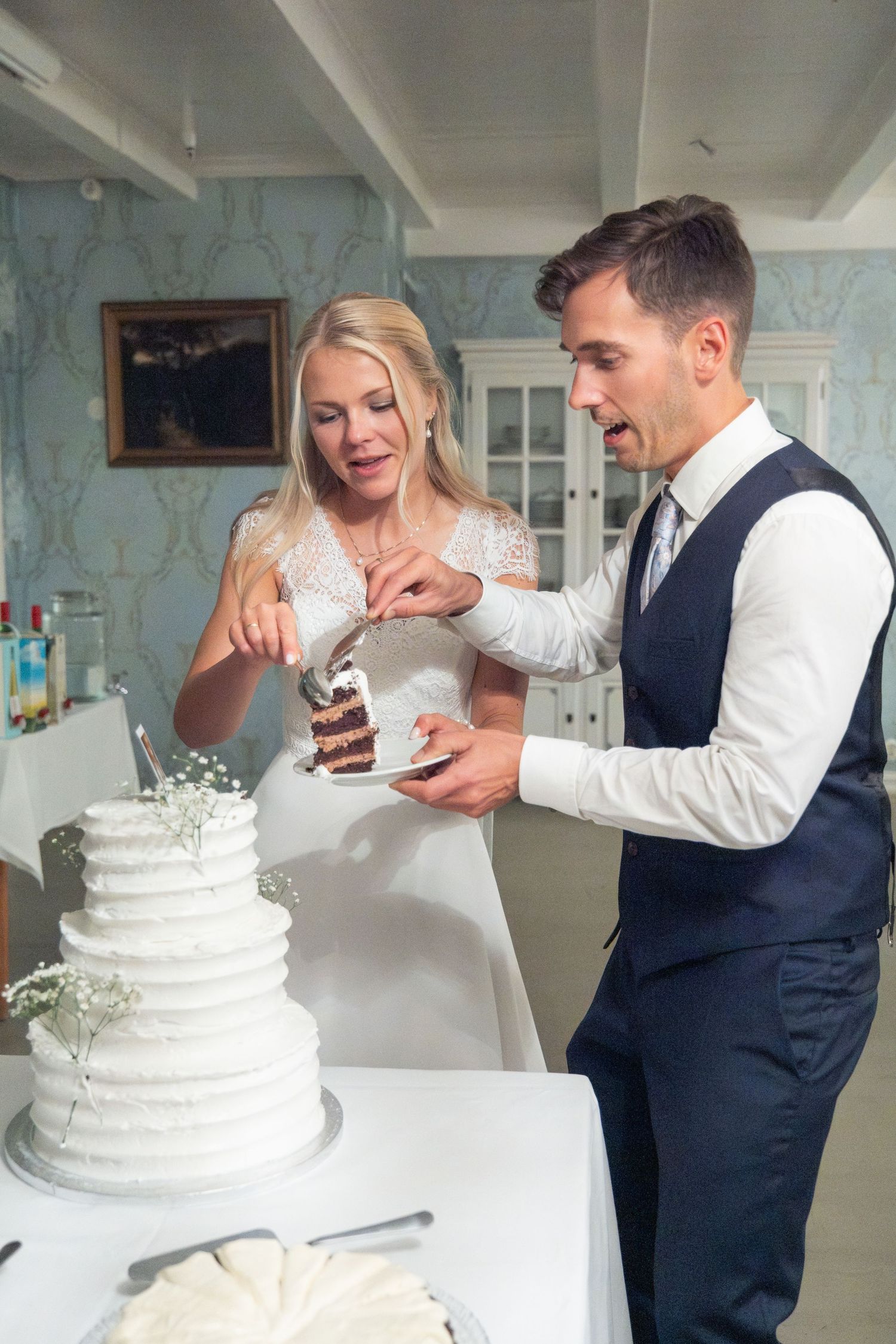 Bride and groom cutting their white tiered wedding cake together at their elegant reception.