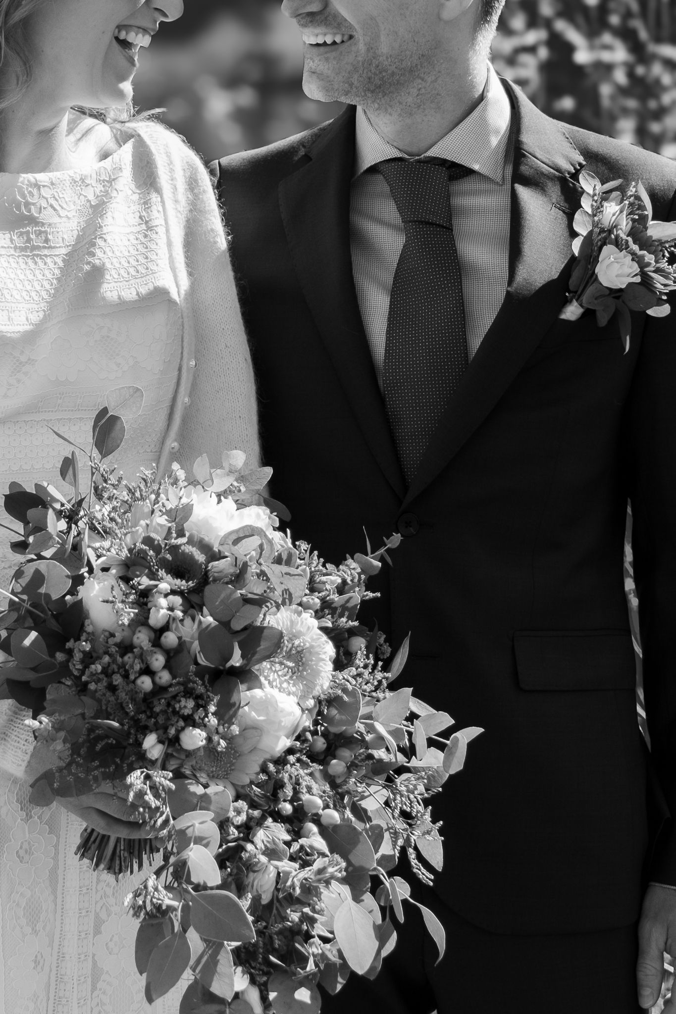 Close-up black and white photo of bride and groom smiling together holding a lush floral wedding bouquet.