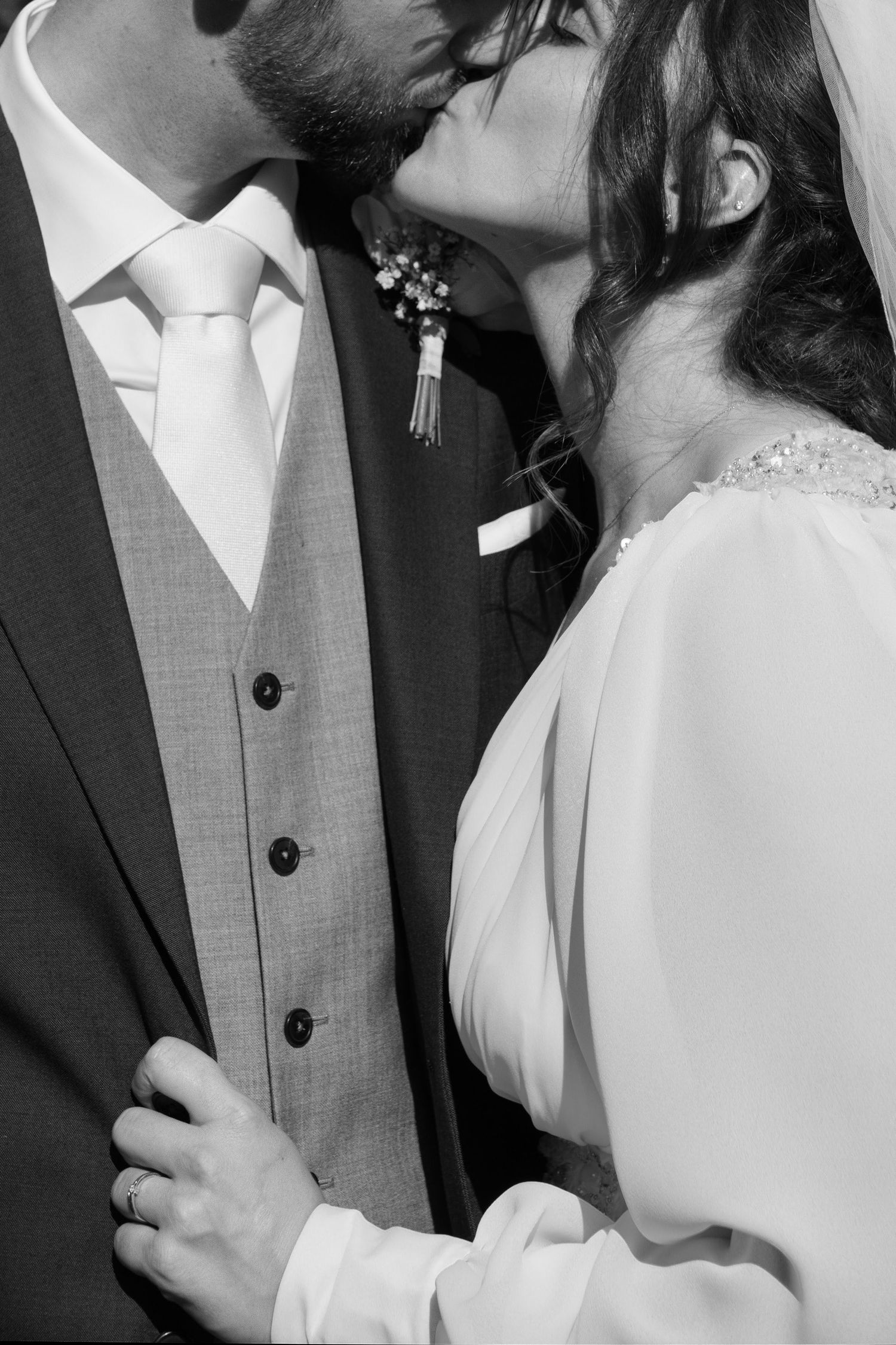 Black and white close-up of bride and groom sharing a kiss, groom wearing boutonniere and vest.