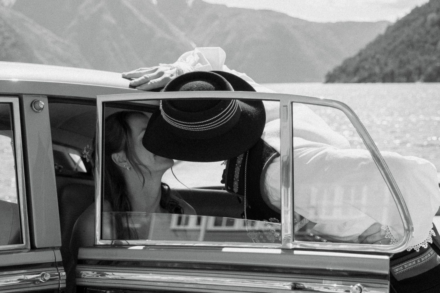 Black and white photo of bride and groom kissing through the window of a vintage classic car.