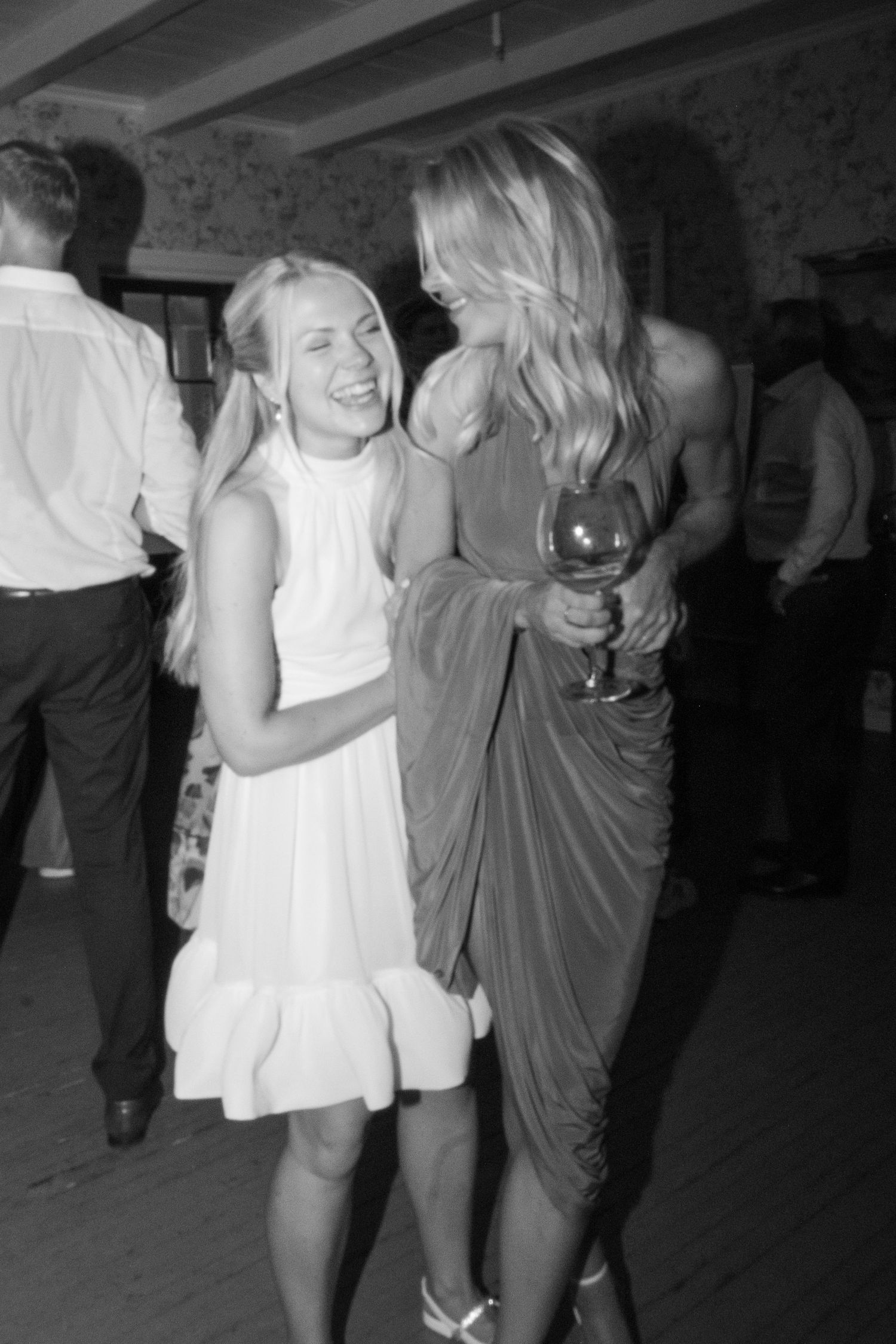 Black and white photo of two women laughing and dancing together at a wedding reception celebration.