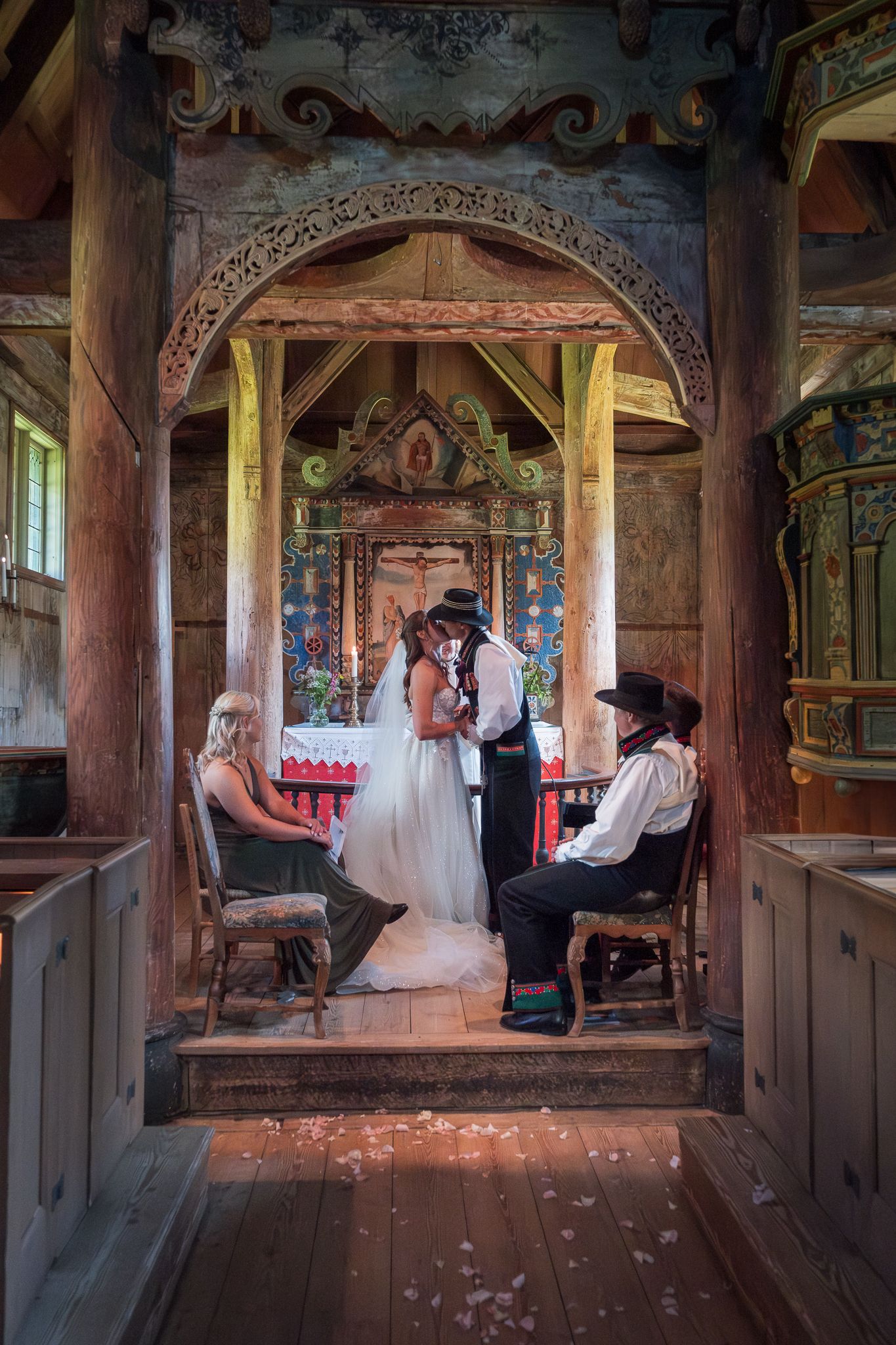 Bride and groom share a kiss at the altar of a richly decorated historic wooden Norwegian stave church.