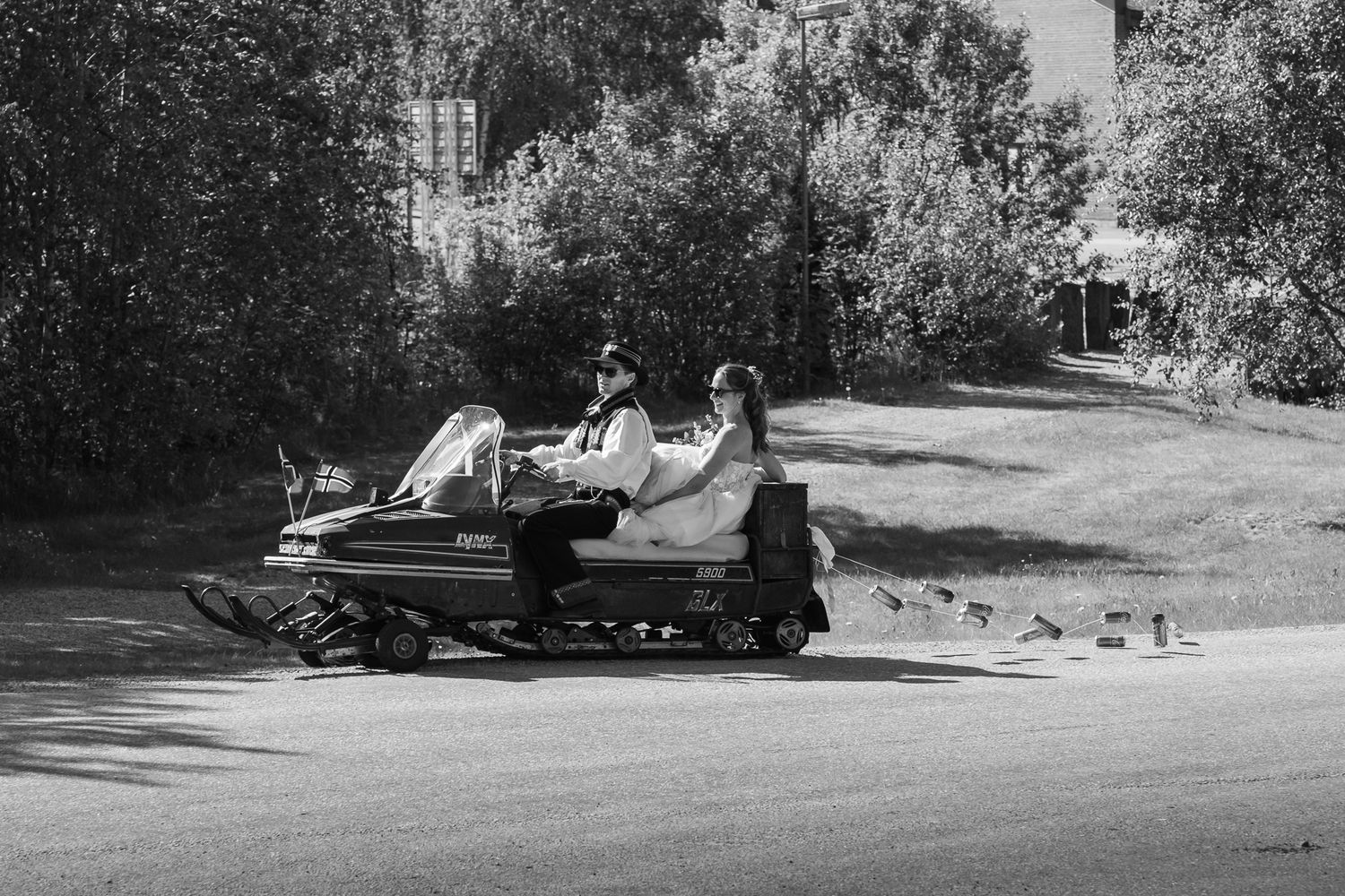 Black and white photo of a bride and groom riding a snowmobile together on a sunny day.