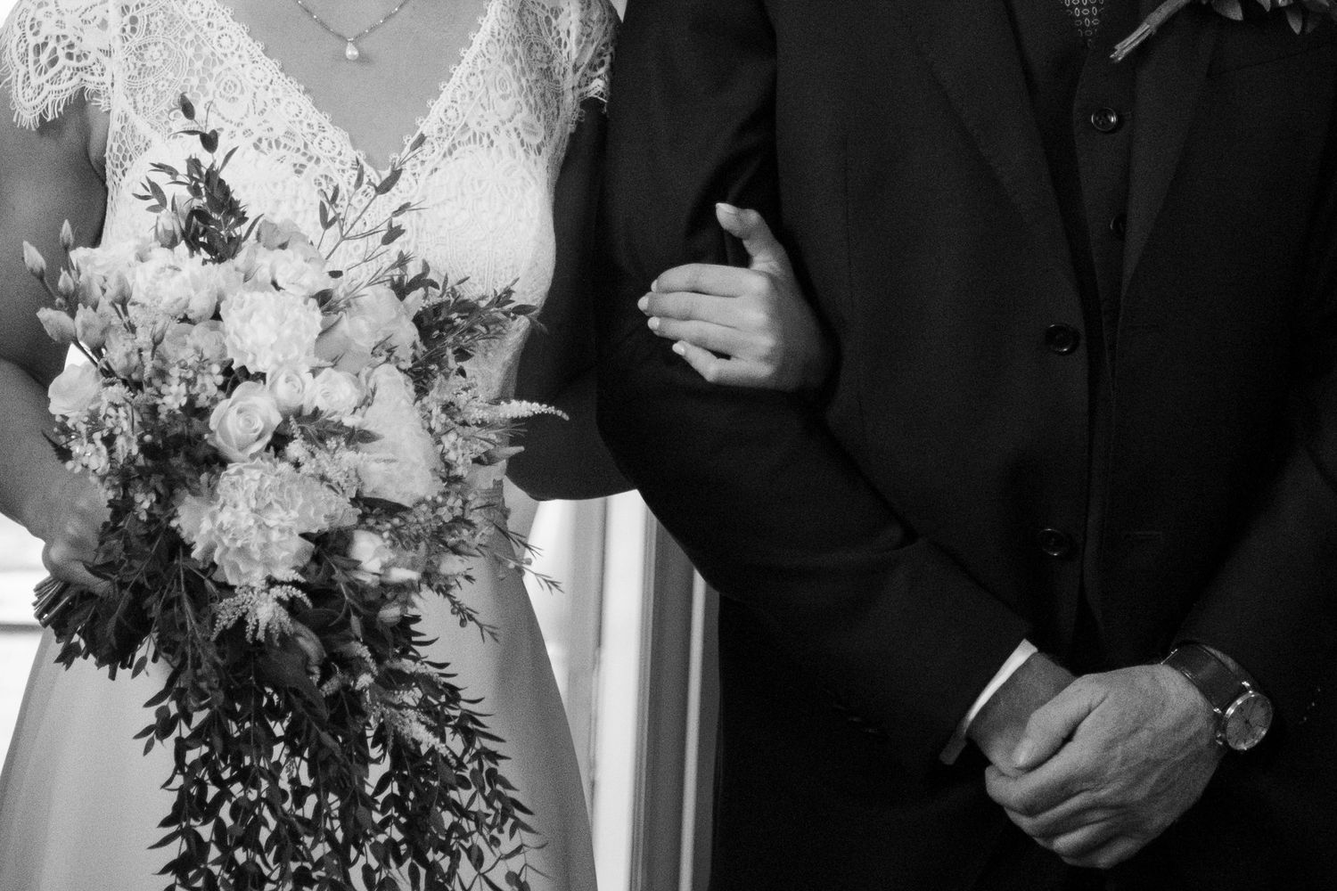 Black and white close-up of a bride holding a floral bouquet while standing beside a suited groom.