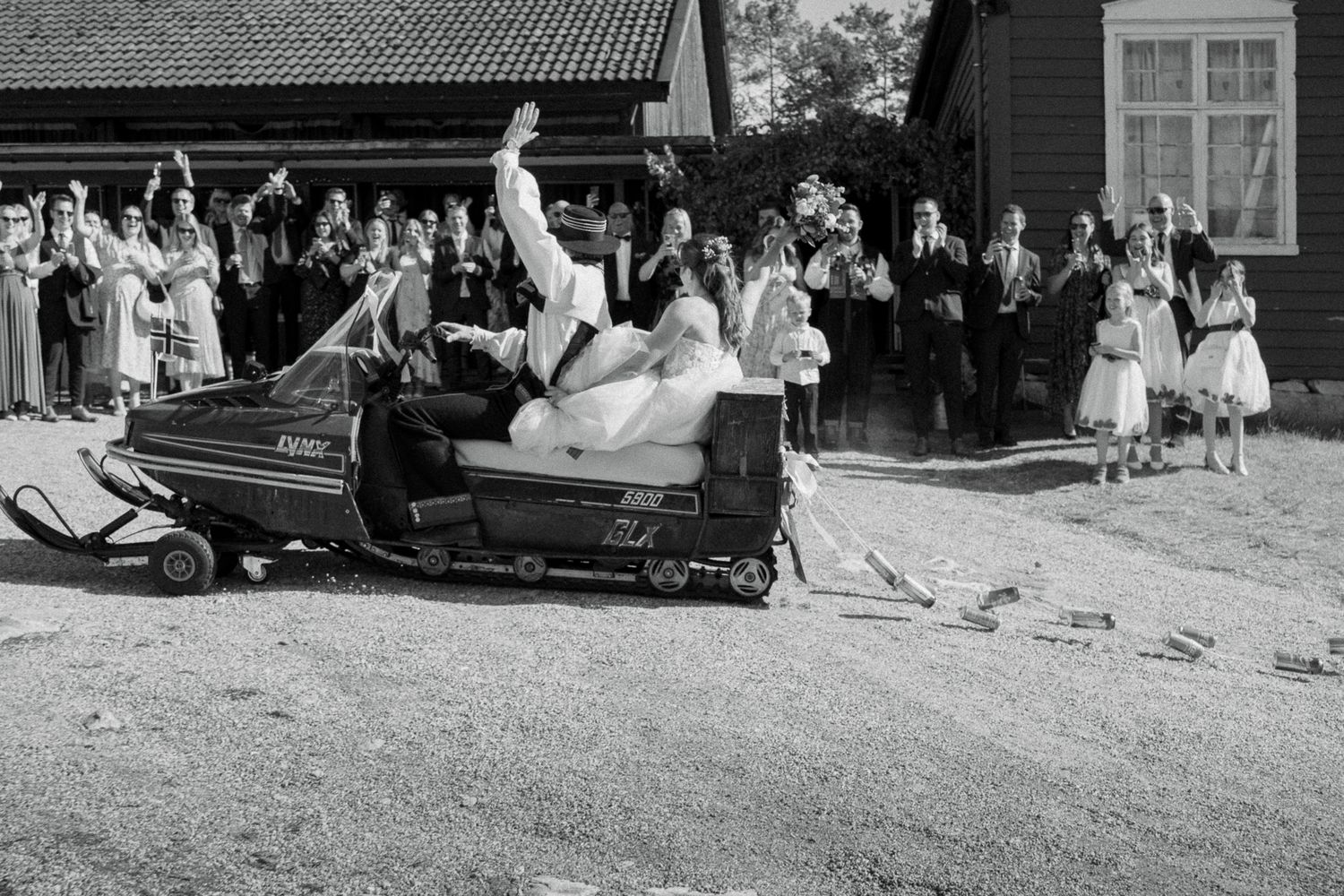 Bride and groom ride a snowmobile at their outdoor wedding while guests celebrate in the background.