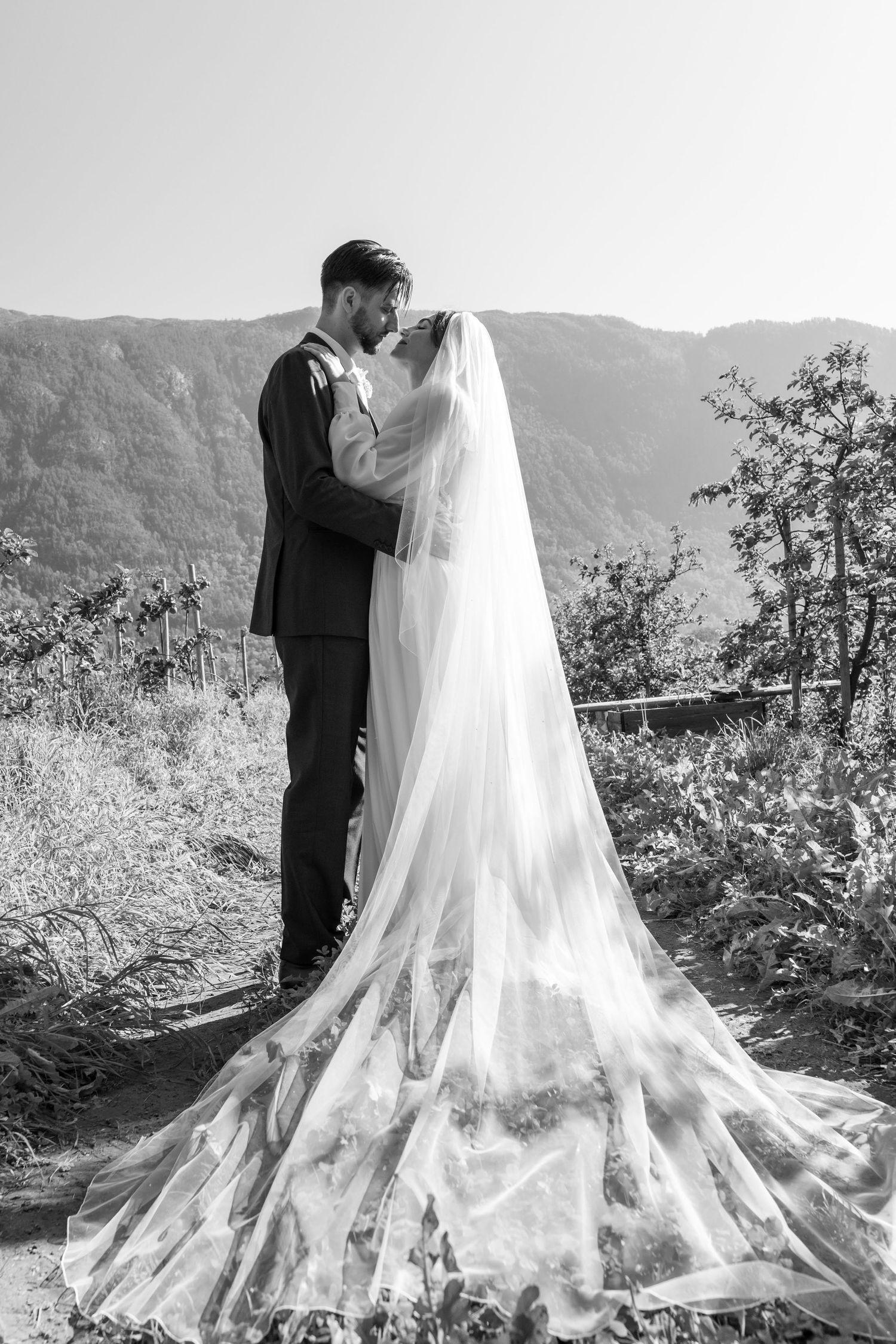 Black and white photo of bride and groom kissing with dramatic mountain landscape in background.