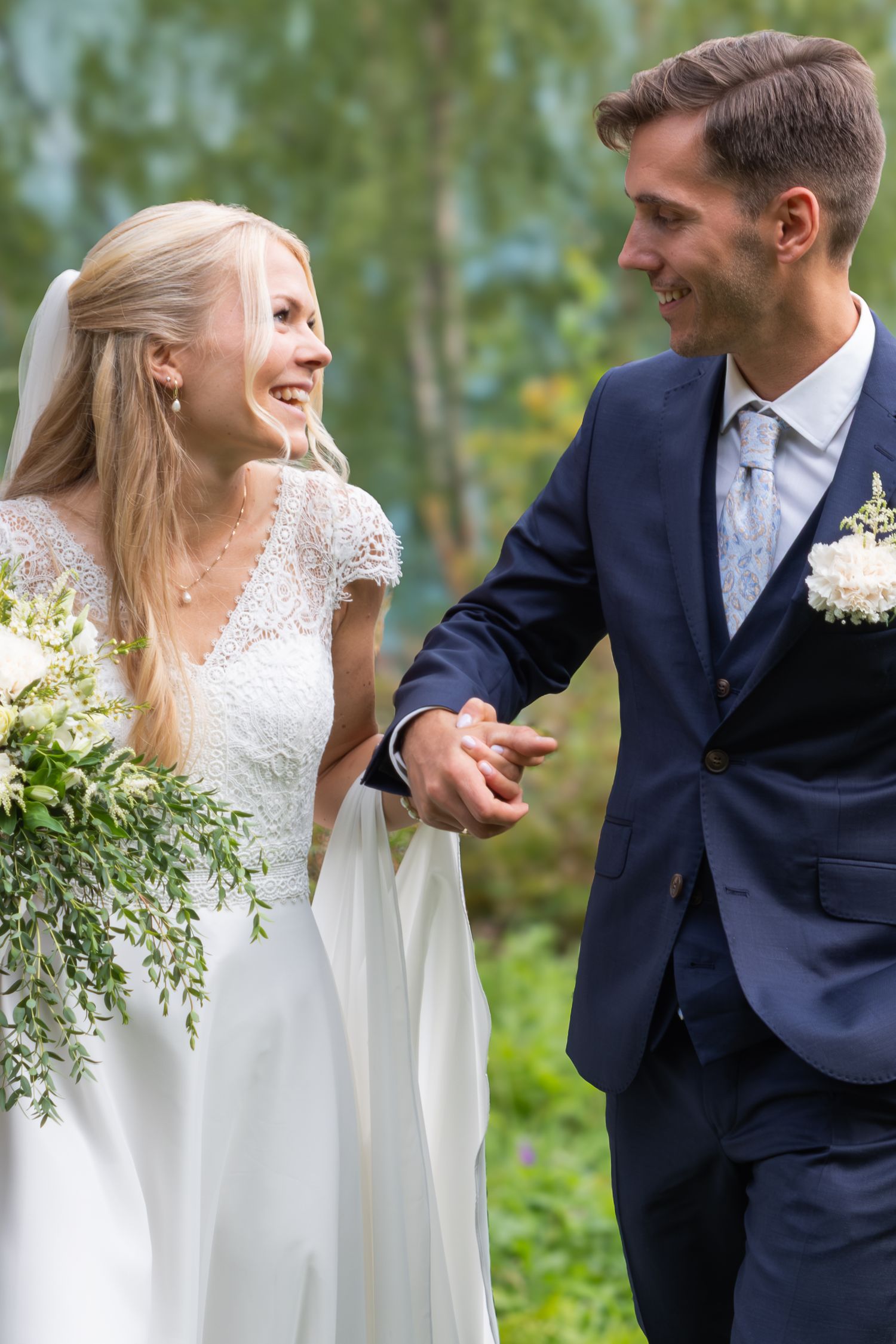 Happy bride and groom holding hands and smiling at each other outdoors after wedding.