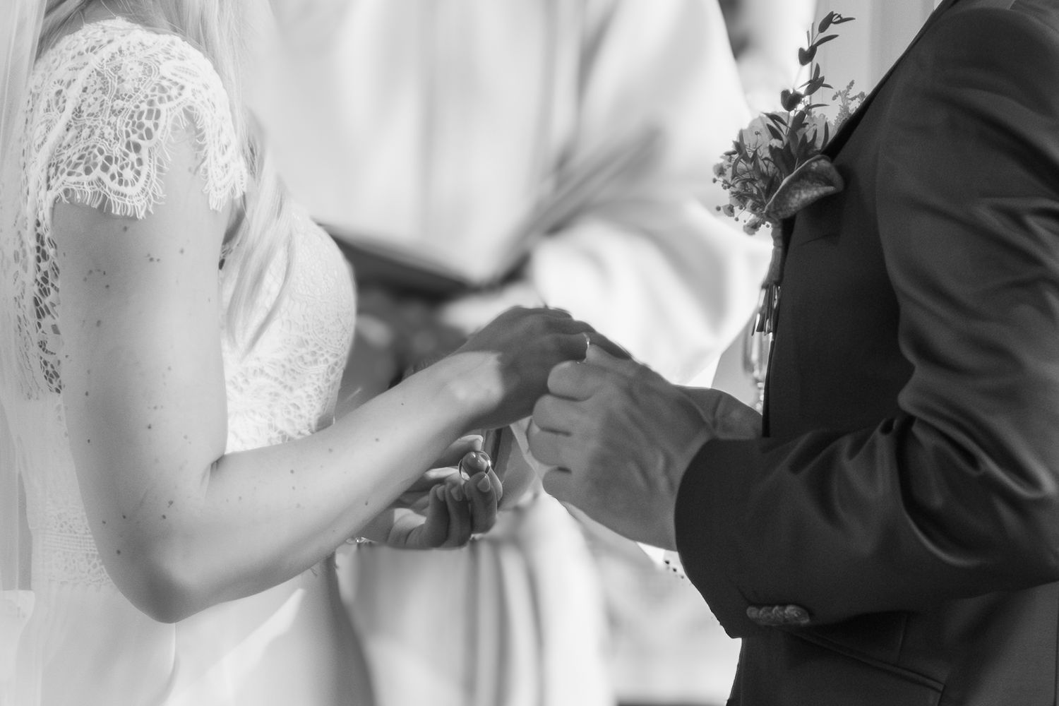 Close-up of groom placing wedding ring on brides finger during ceremony in black and white.