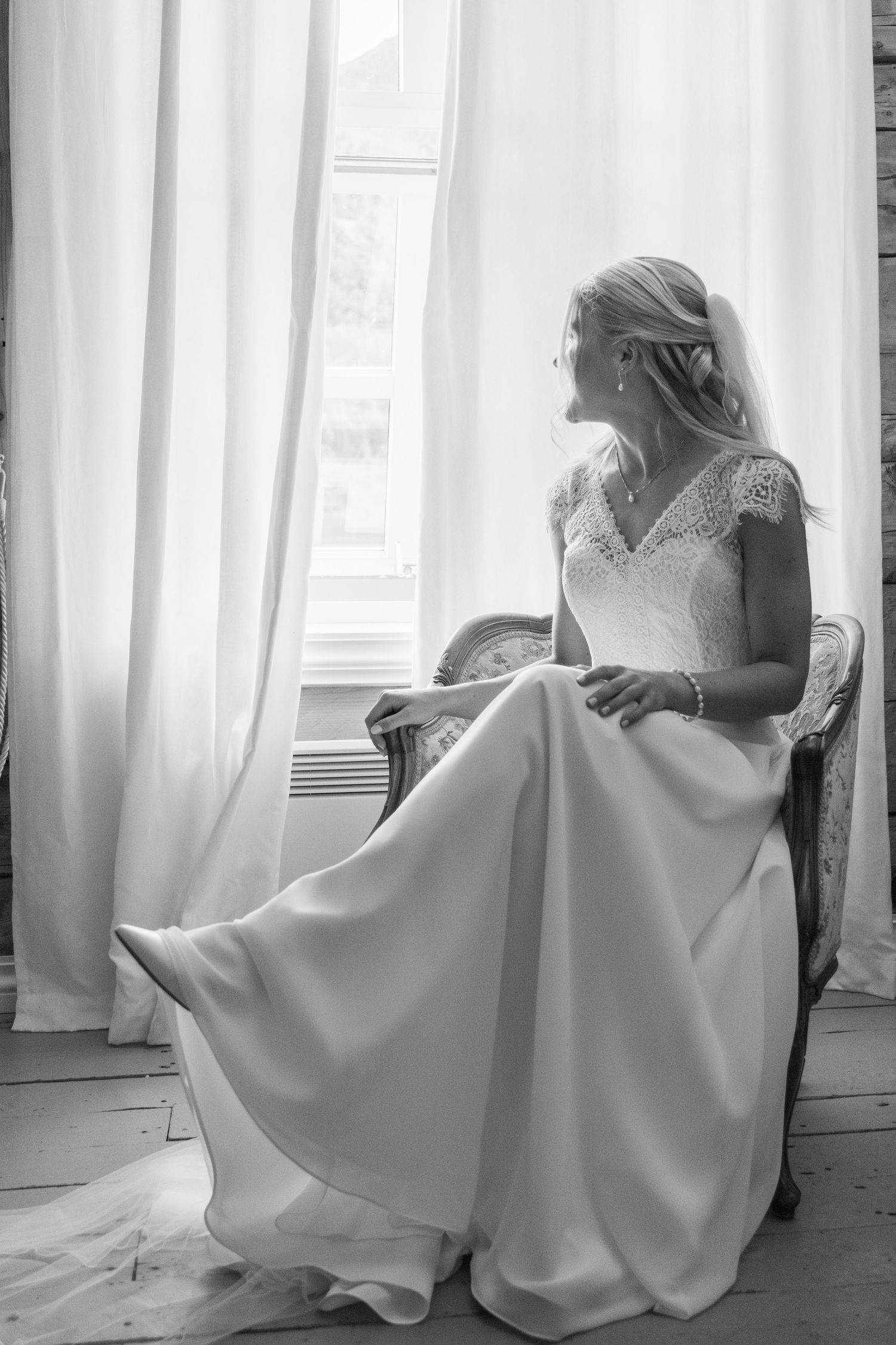 Bride in white wedding dress seated by window in soft natural light.