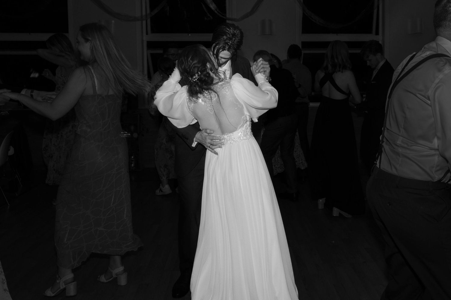 Black and white photo of a bride in a white gown dancing with guests at a wedding reception.