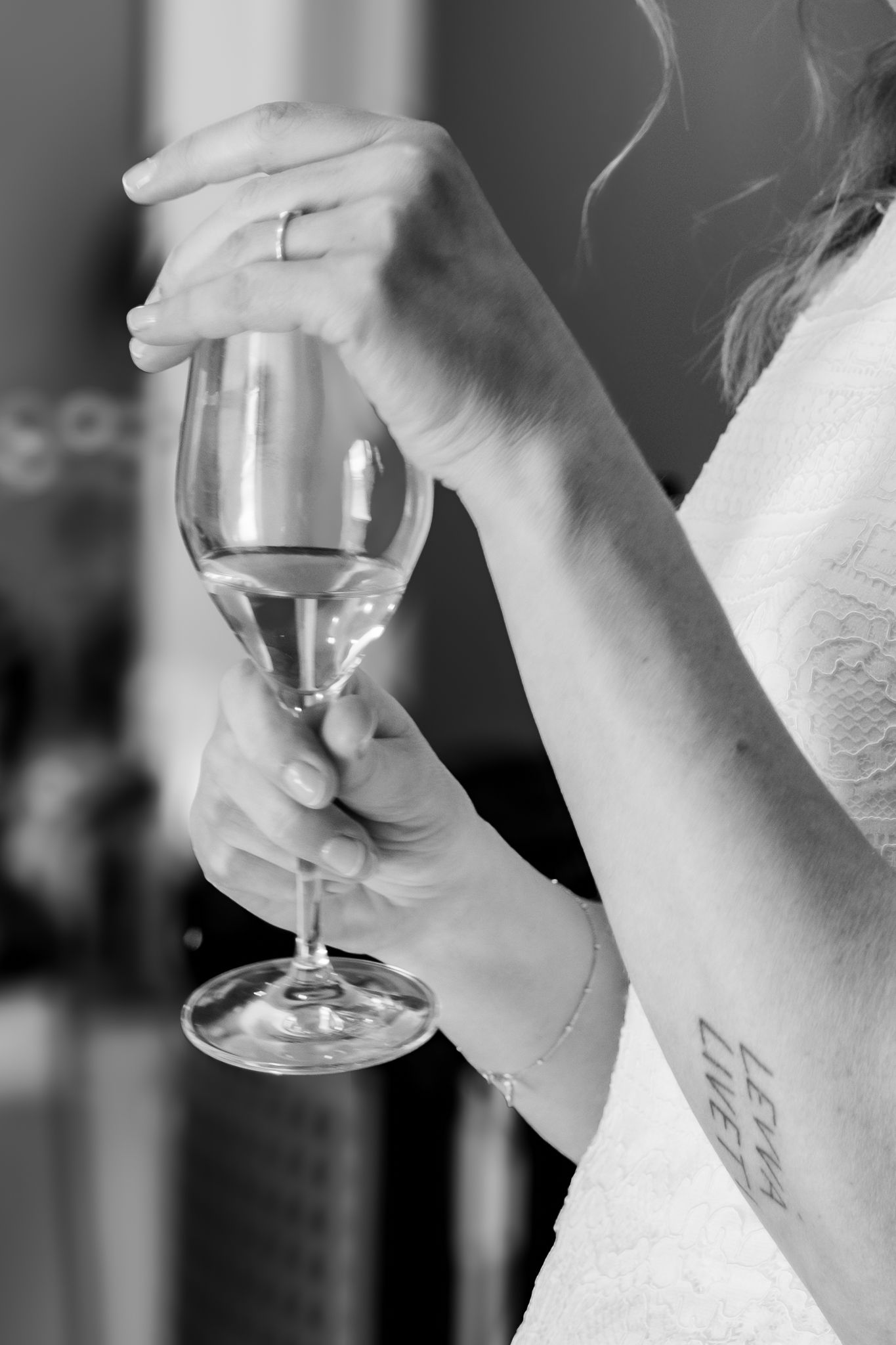 Black and white close-up of bride holding a champagne glass with a wrist tattoo visible.