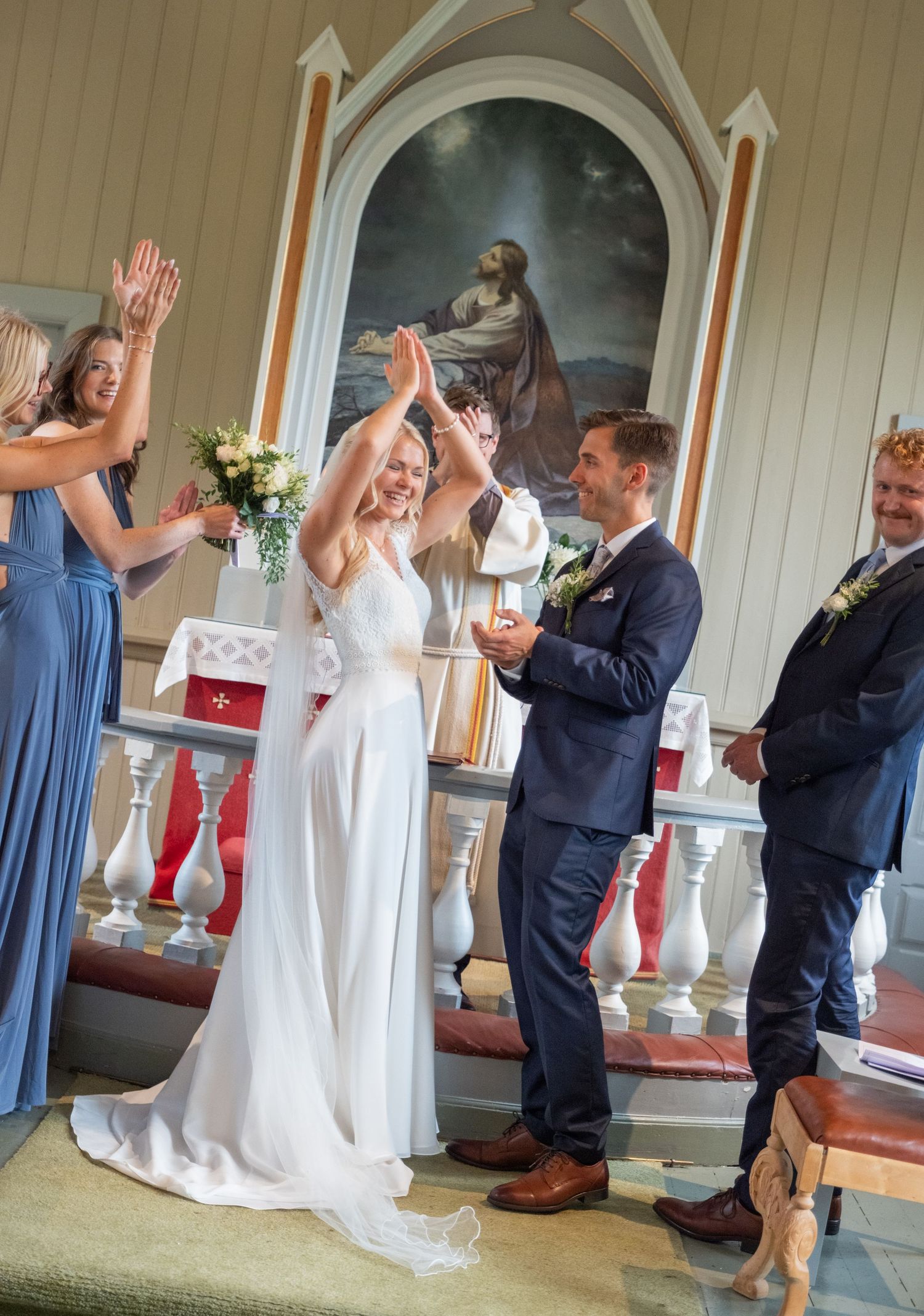 Joyful bride and groom celebrate at church altar with raised hands surrounded by wedding party.