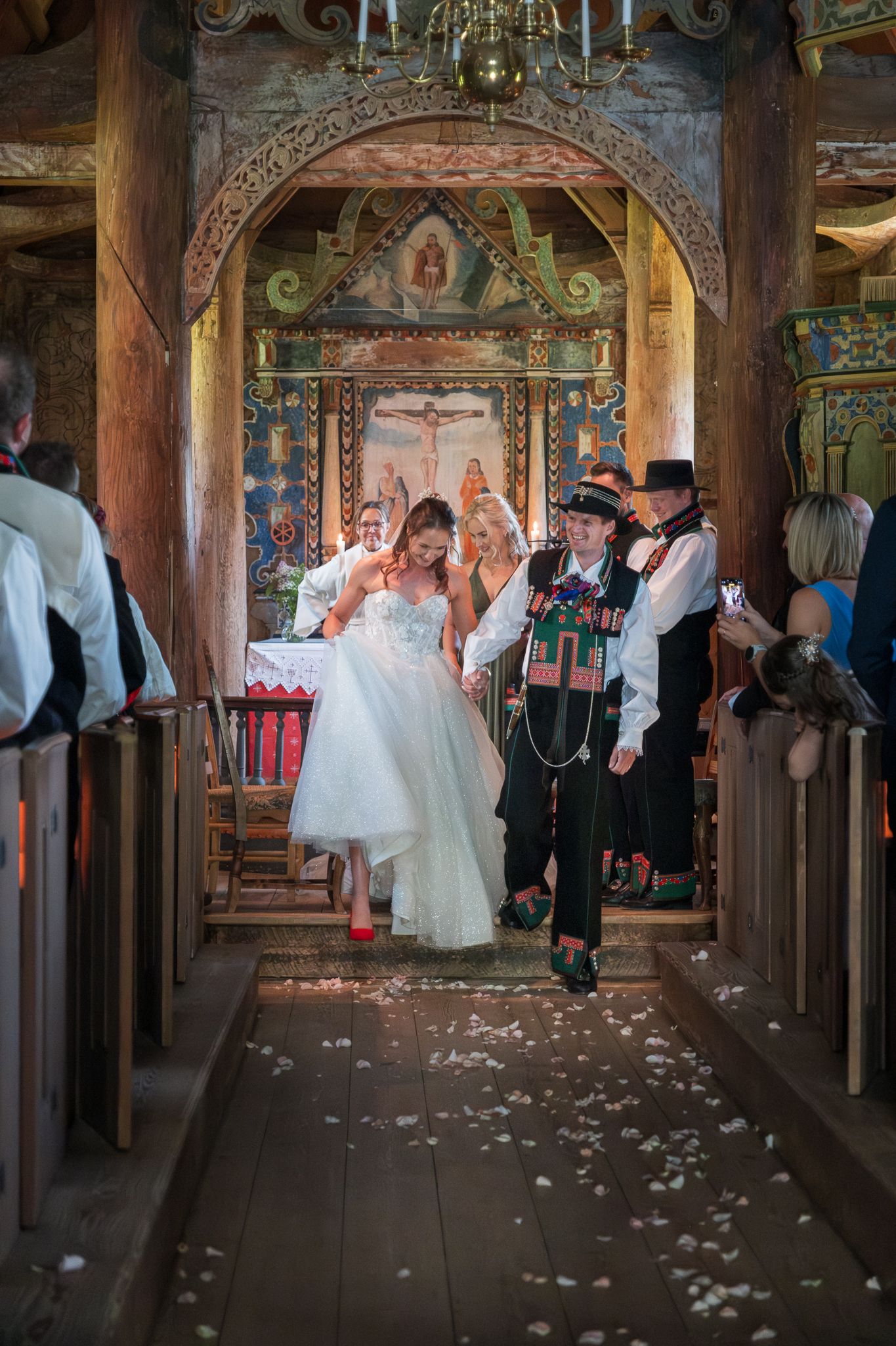 Newlyweds joyfully walk back down the aisle in a colorful historic wooden church after their wedding ceremony.