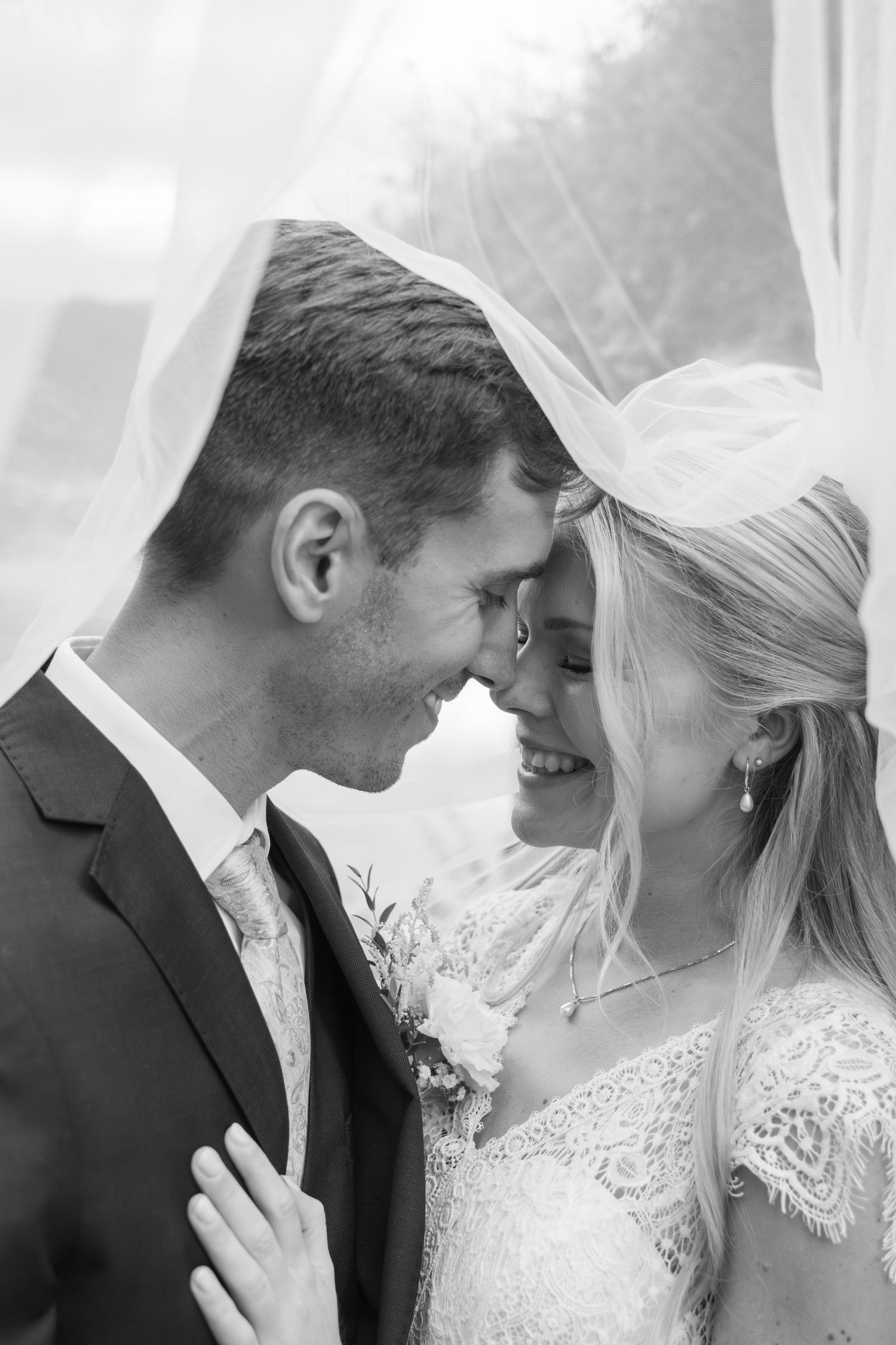 Black and white close-up of laughing bride and groom sharing a joyful moment under the wedding veil.