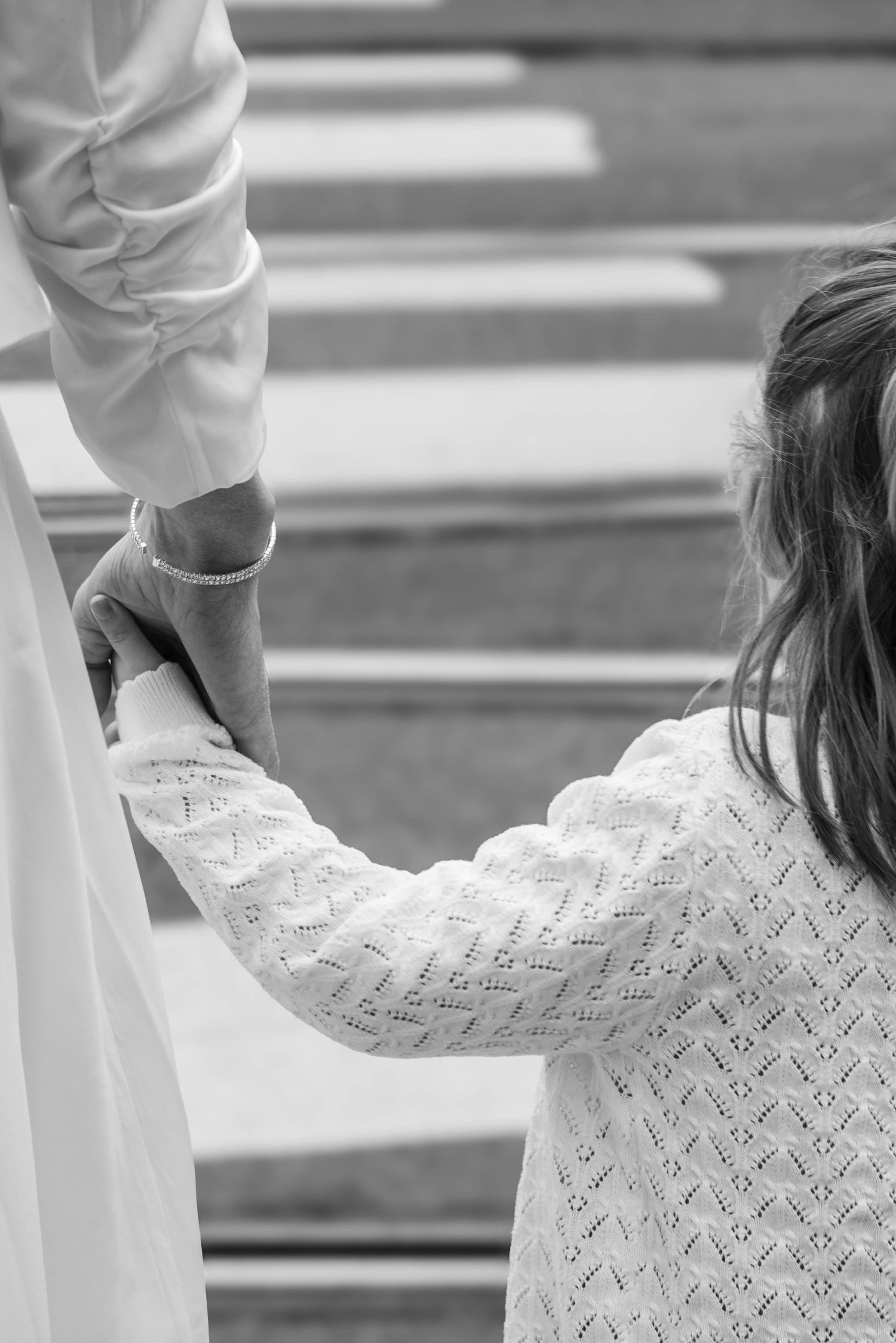 Black and white close-up of bride and groom holding hands on a staircase, showcasing delicate lace sleeve detail.