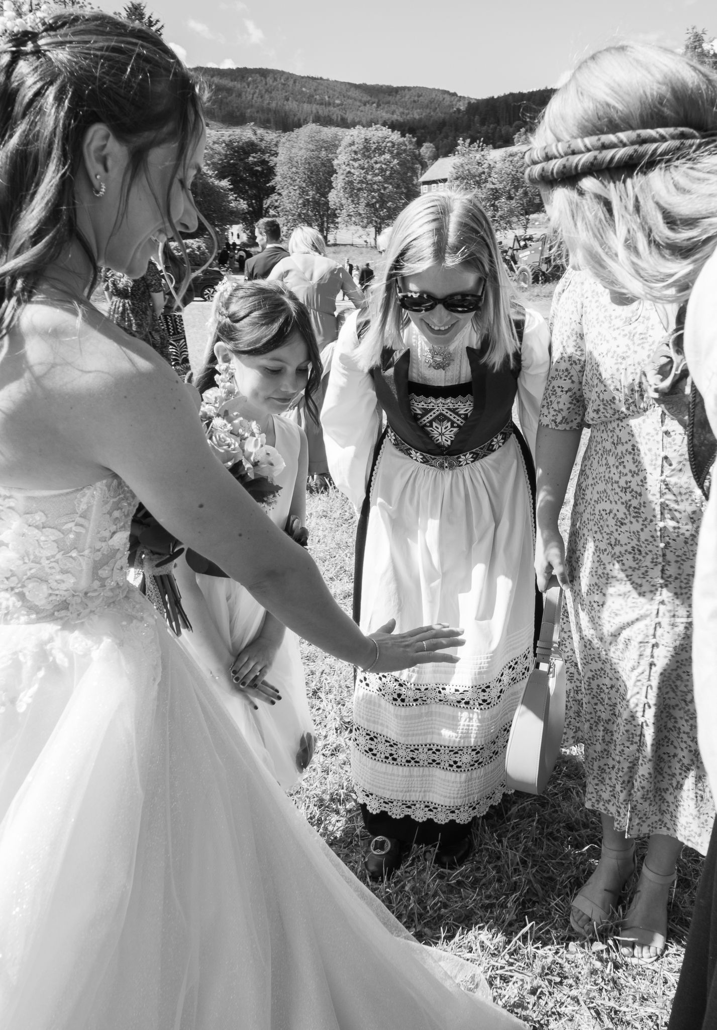 Bride in white gown interacting with a young girl in traditional Norwegian dress at an outdoor wedding.