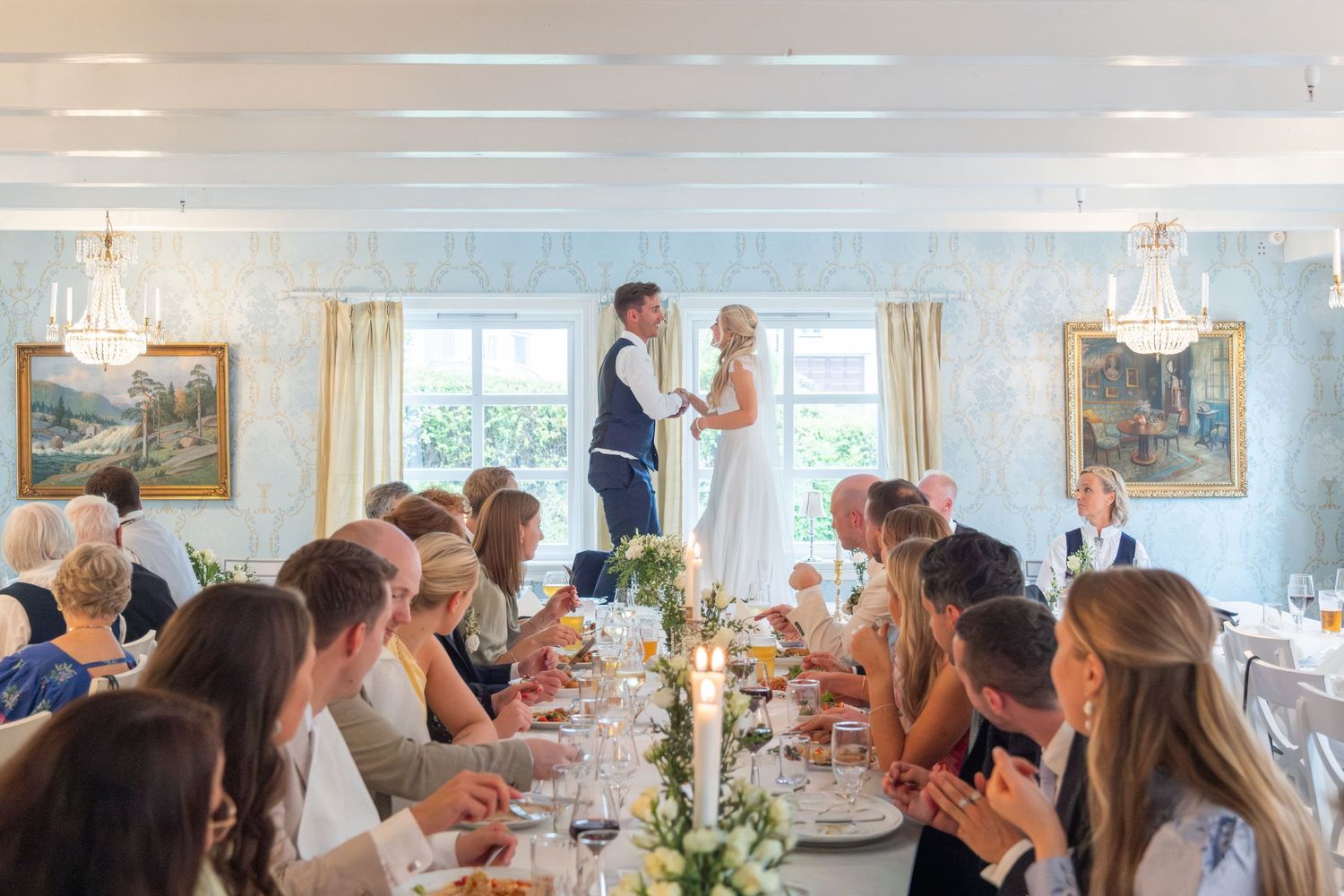 Newlyweds share a romantic moment standing at their wedding reception dinner table.
