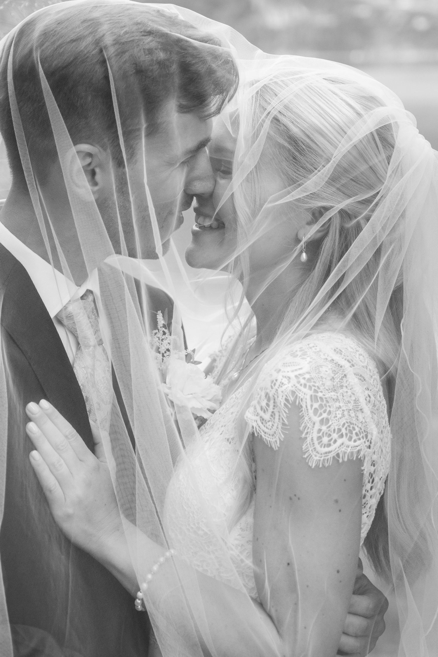 Romantic black and white portrait of bride and groom sharing intimate moment under wedding veil.