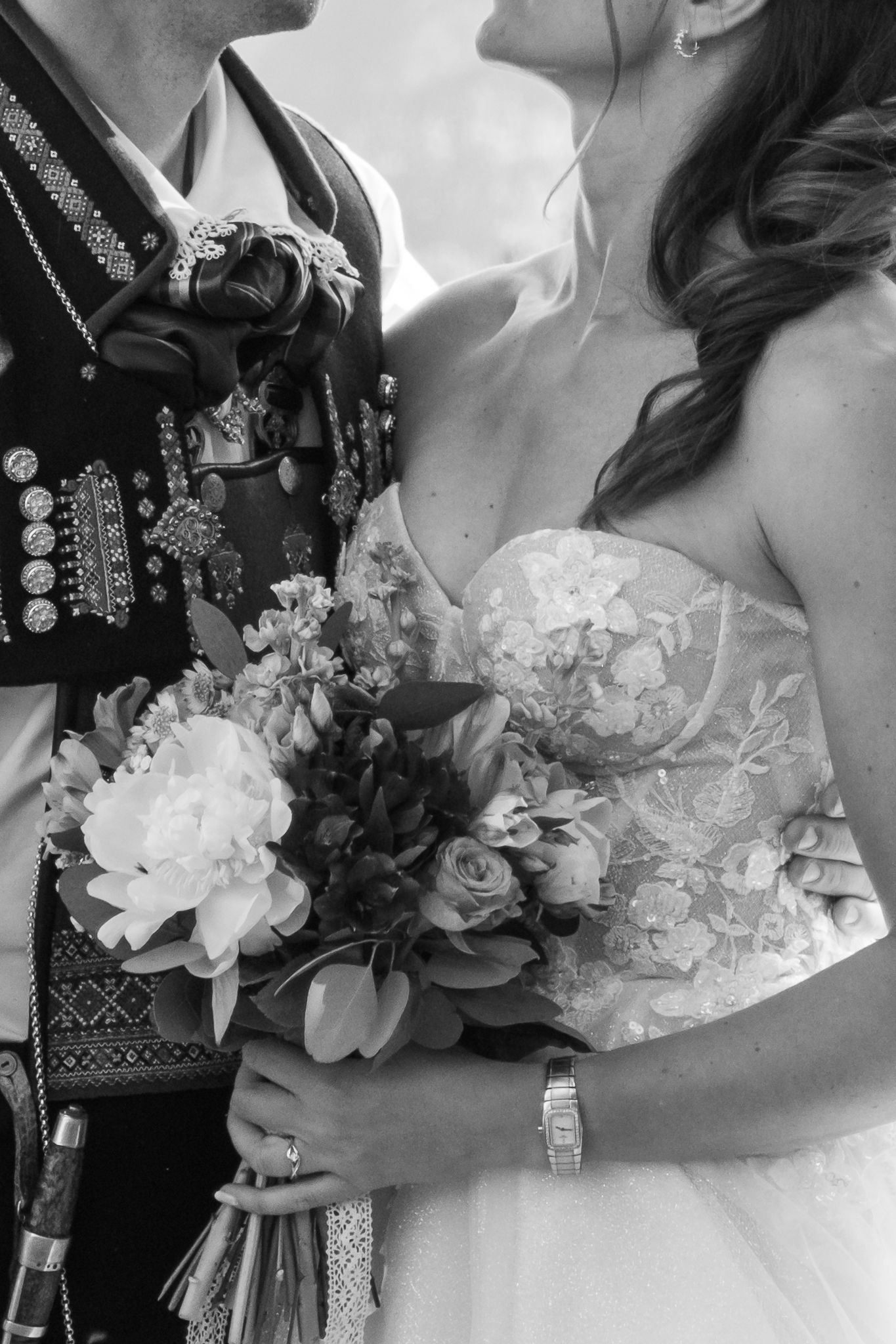 Close-up black and white photo of bride and groom in Norwegian bunad holding a beautiful floral wedding bouquet.
