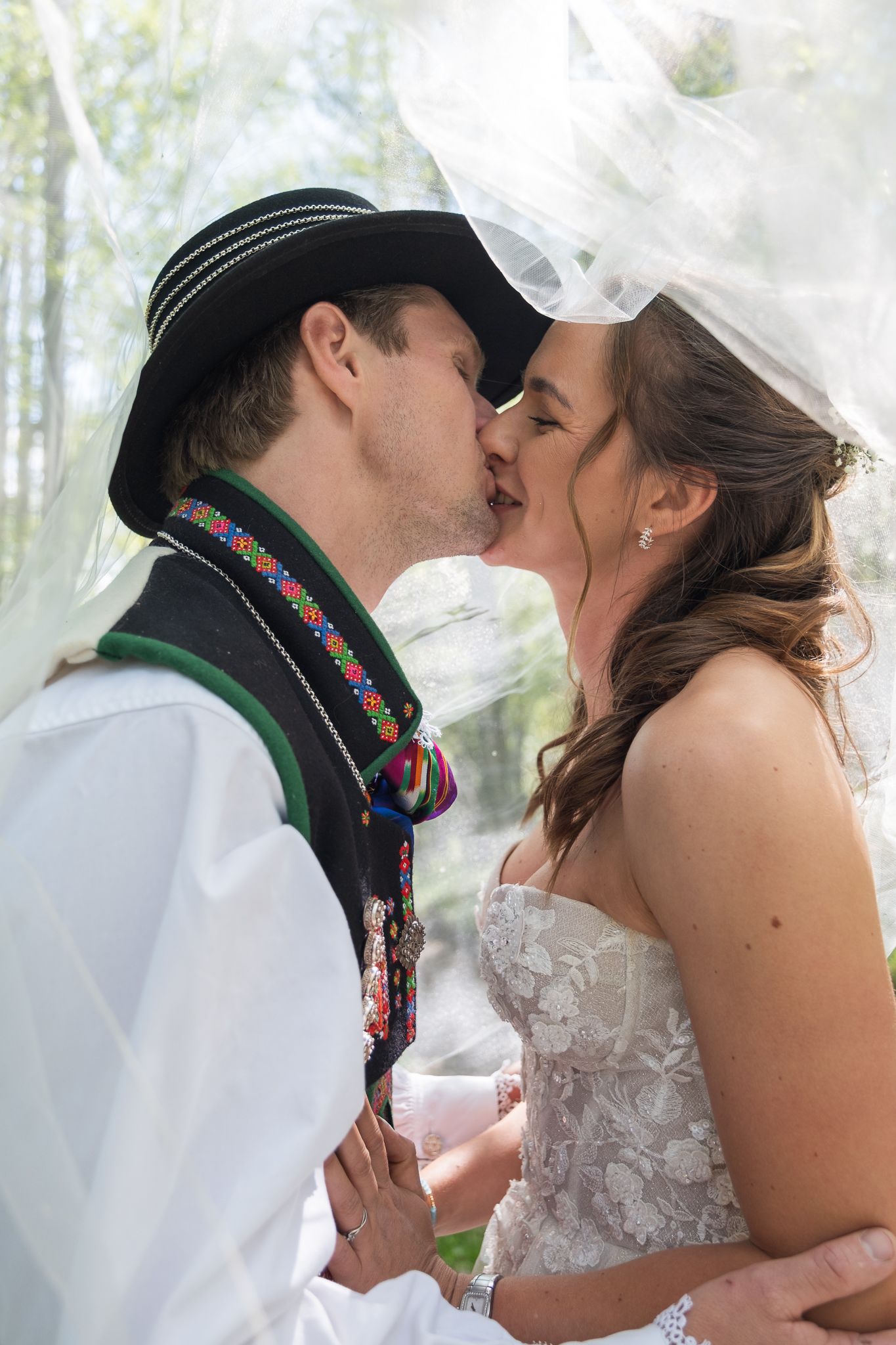 Bride and groom sharing a tender kiss under a flowing veil in a softly lit outdoor setting.