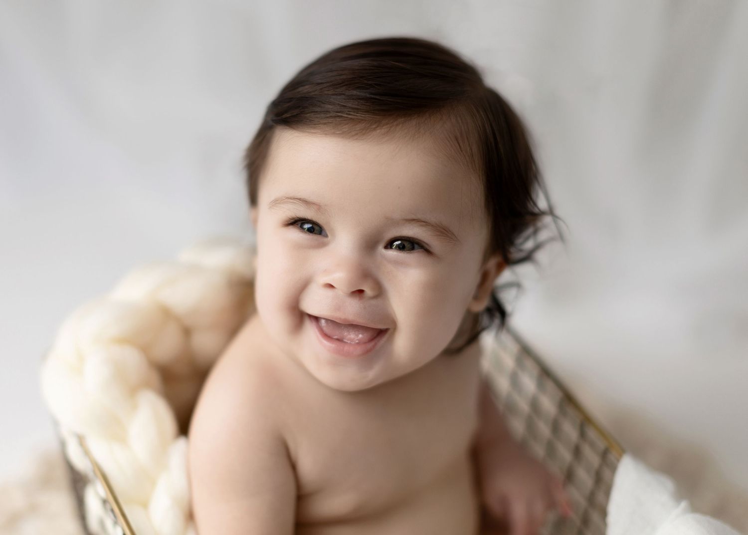 Happy baby smiling while lying in cream-colored basket.