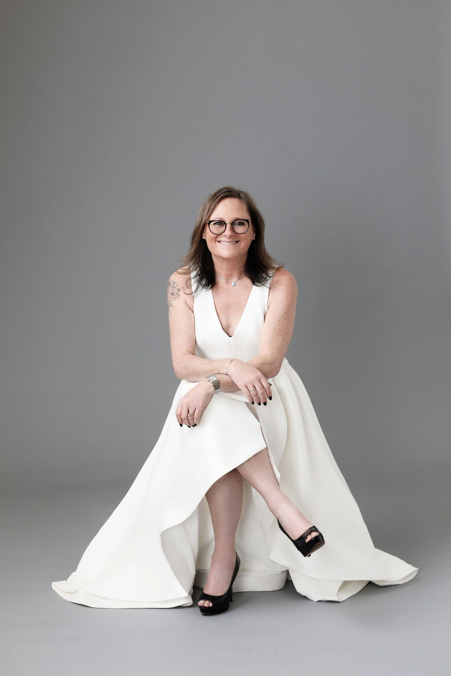 Woman in white dress poses elegantly on floor against grey studio background.