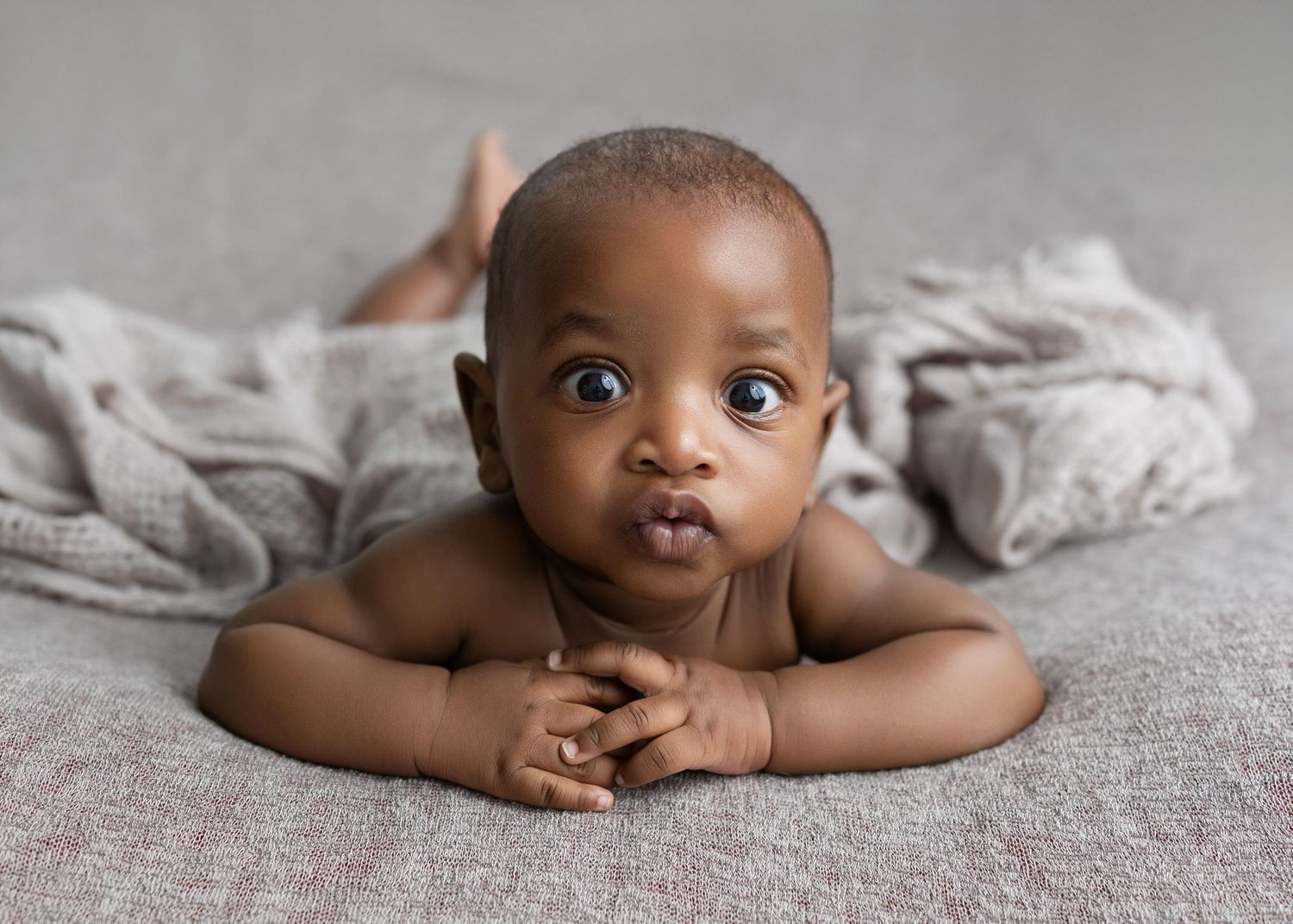 Baby lying on soft grey blanket showing expressive eyes and facial expressions in studio portraits.