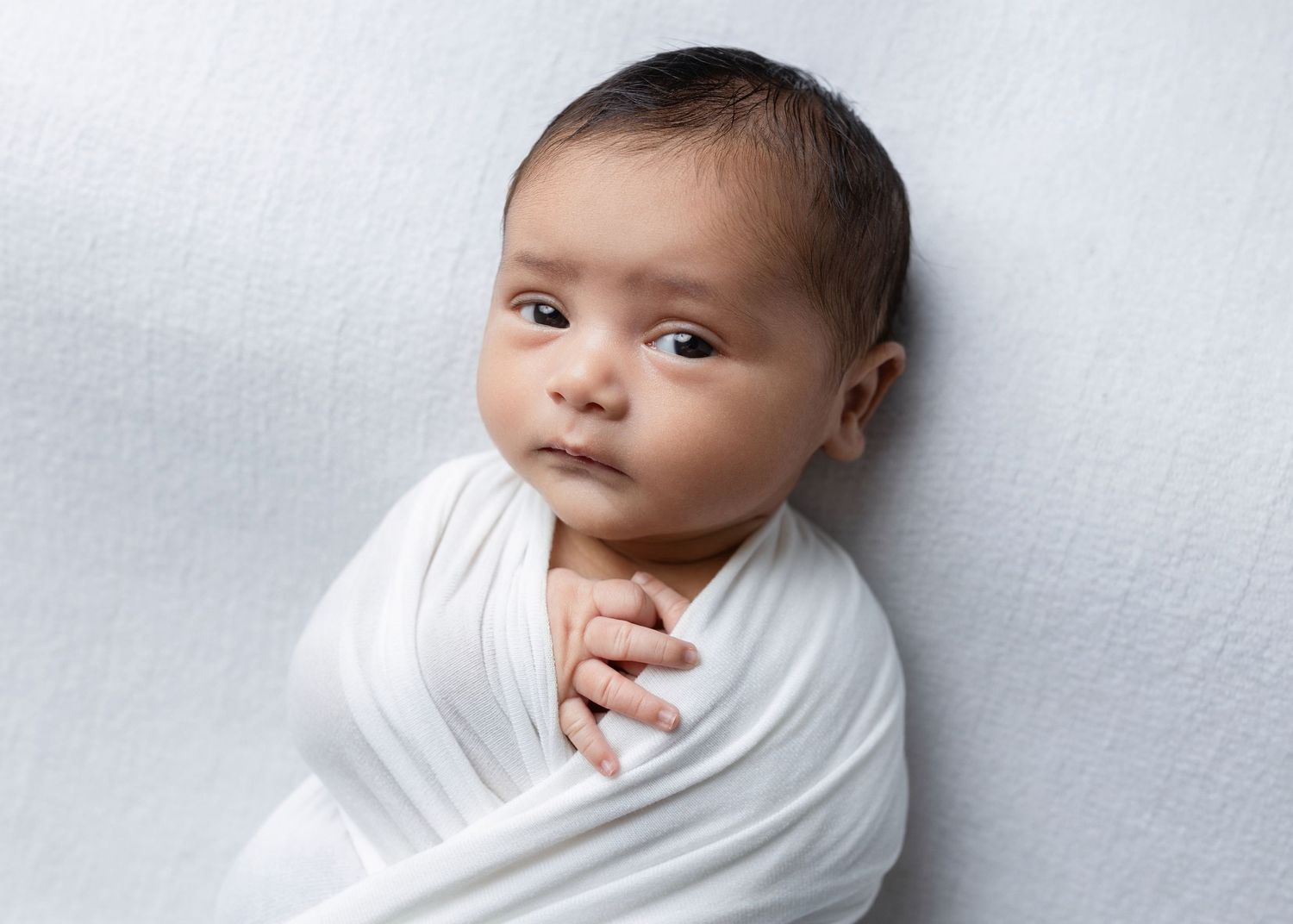 A newborn baby wrapped in white fabric is photographed in multiple poses against a light gray background.