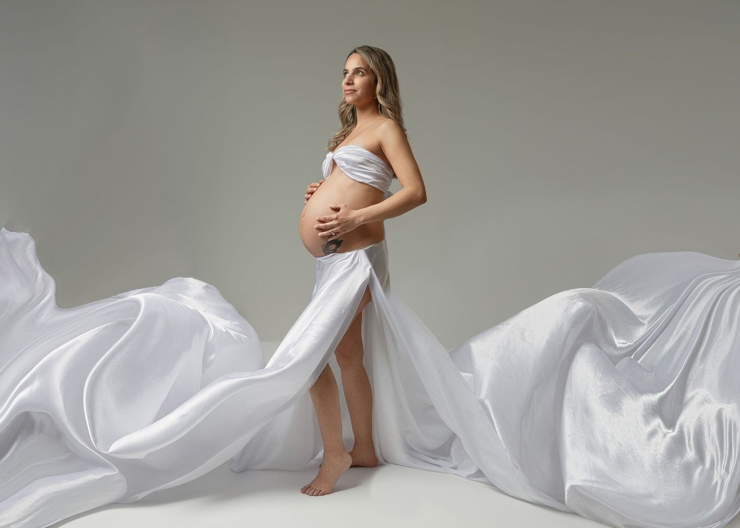 Graceful maternity photo featuring flowing white fabric and artistic pose.