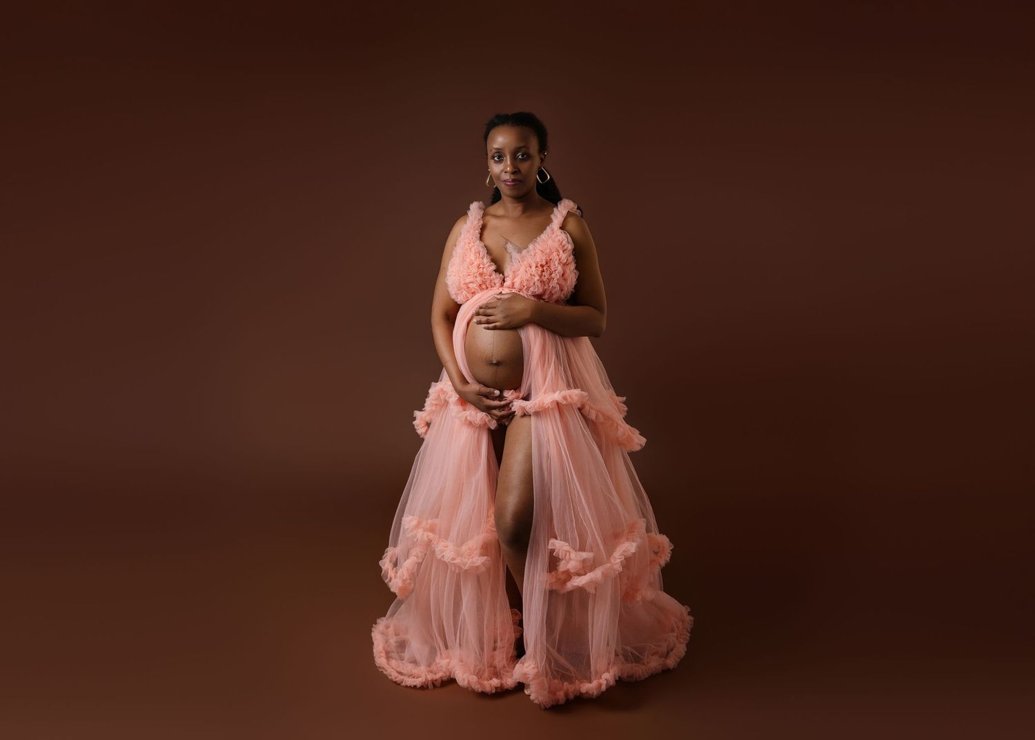 Elegant maternity portraits with pink gown against dark brown background.