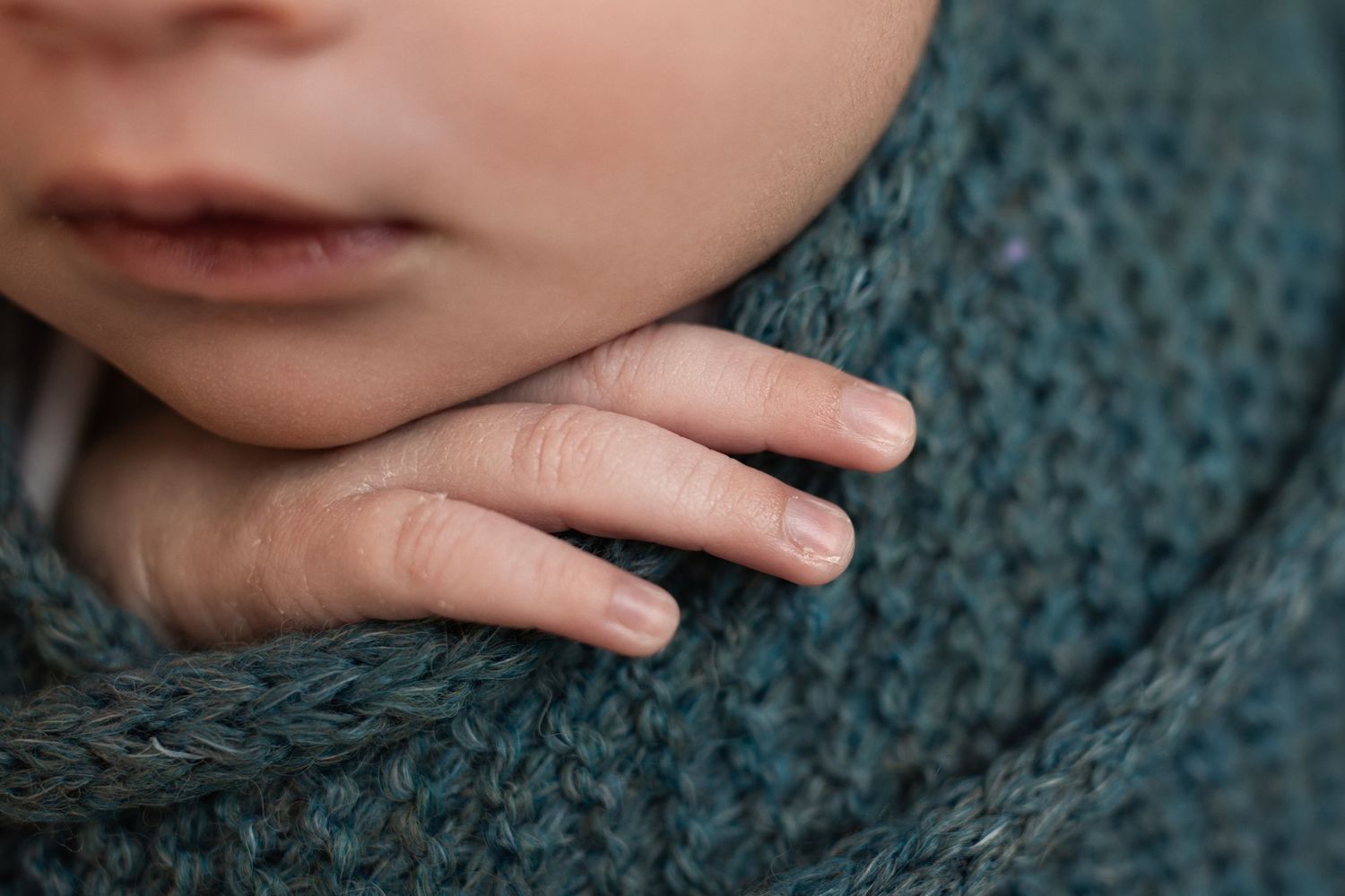 Small hand resting on a cozy teal knit sweater in soft natural lighting.