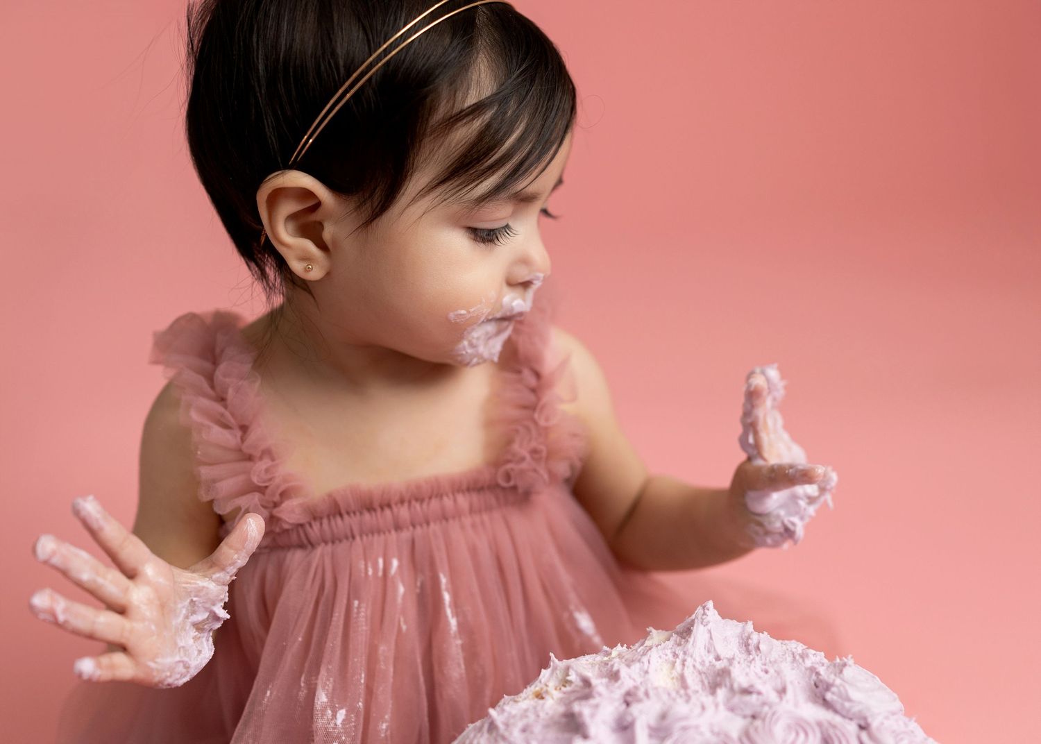 Baby in pink ruffled dress twirls during portrait session against coral background.