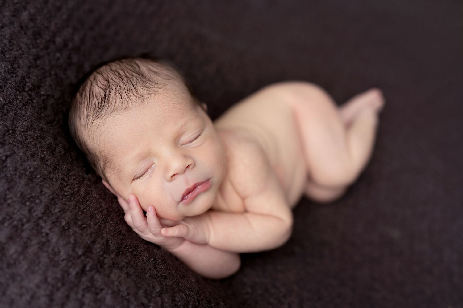 Sleeping newborn posed on dark textured backdrop in artistic style.