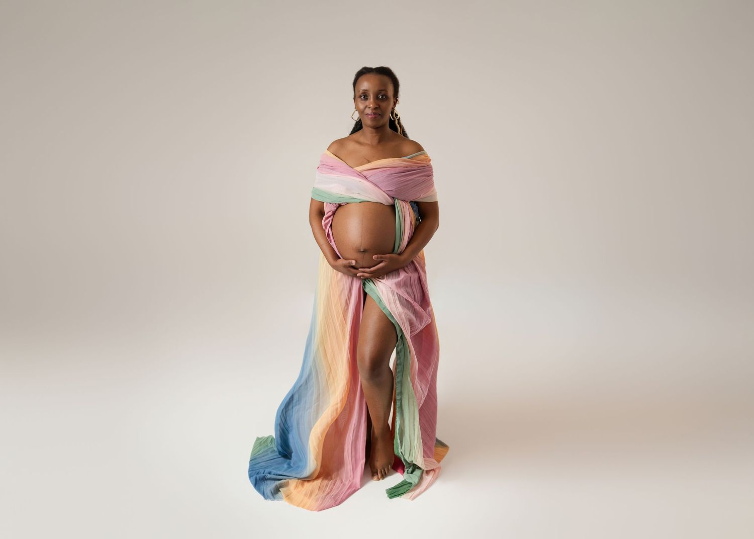 Maternity portraits featuring rainbow pastel dress against neutral backdrop.