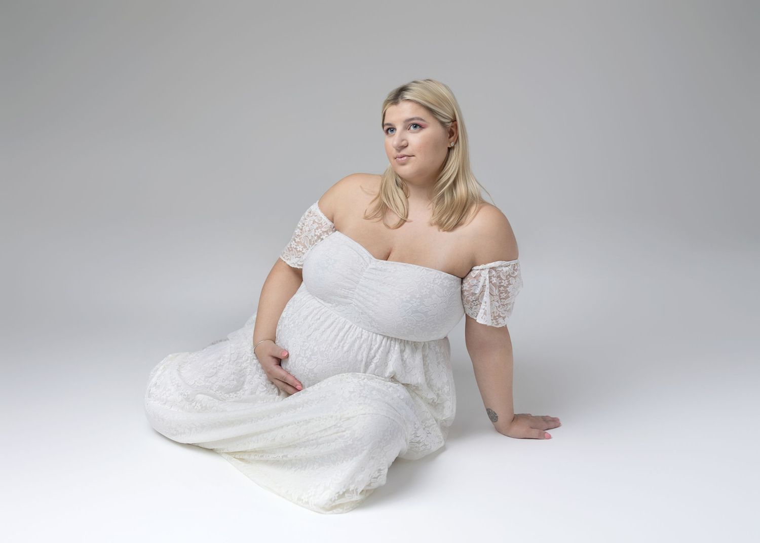 Artistic maternity poses showcasing white lace gown in studio setting.