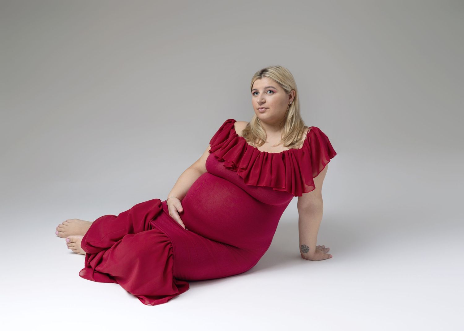 Elegant maternity poses in a flowing burgundy dress on light gray background.