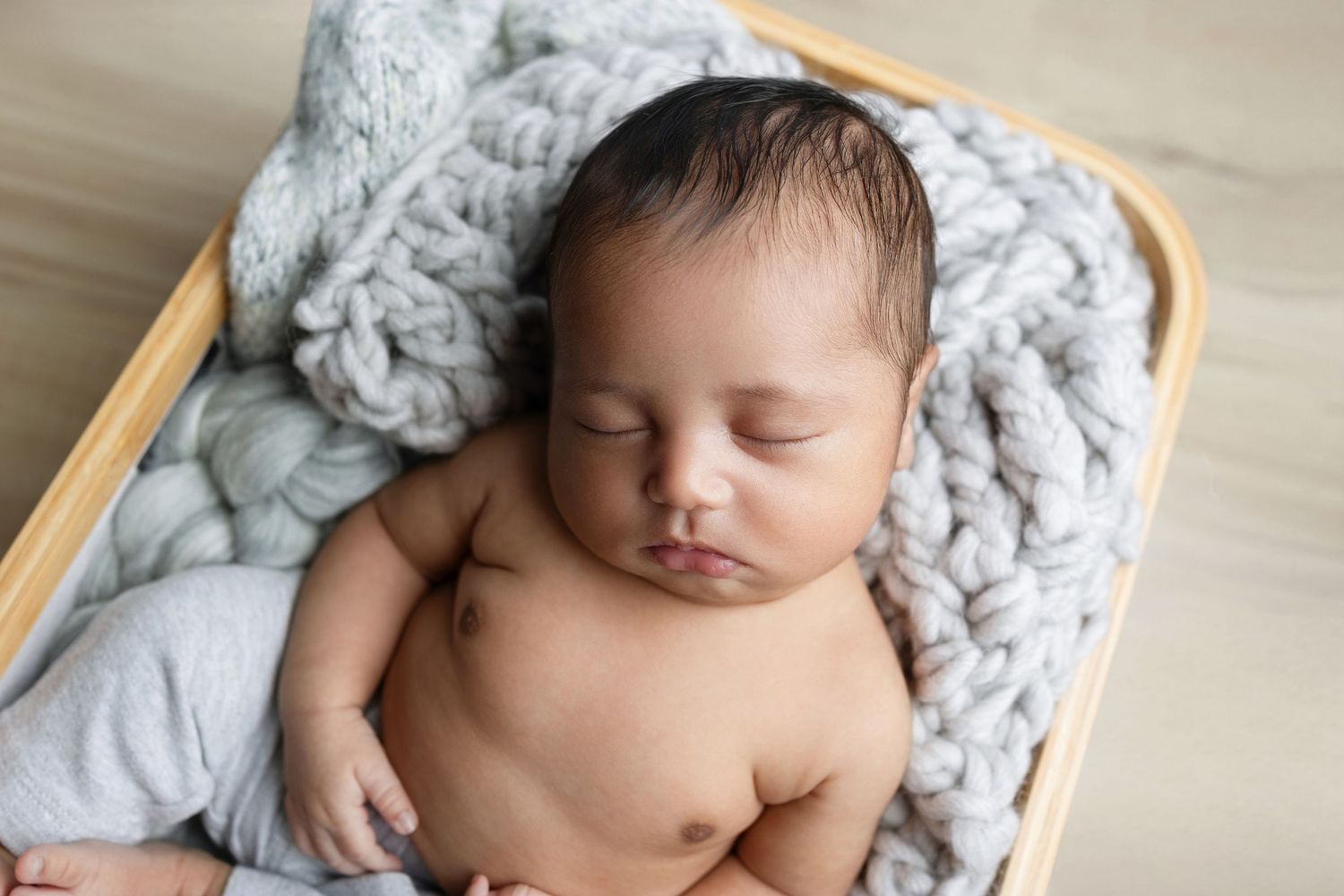 Peaceful sleeping newborn baby lying in wooden basket with soft gray knitted blanket.