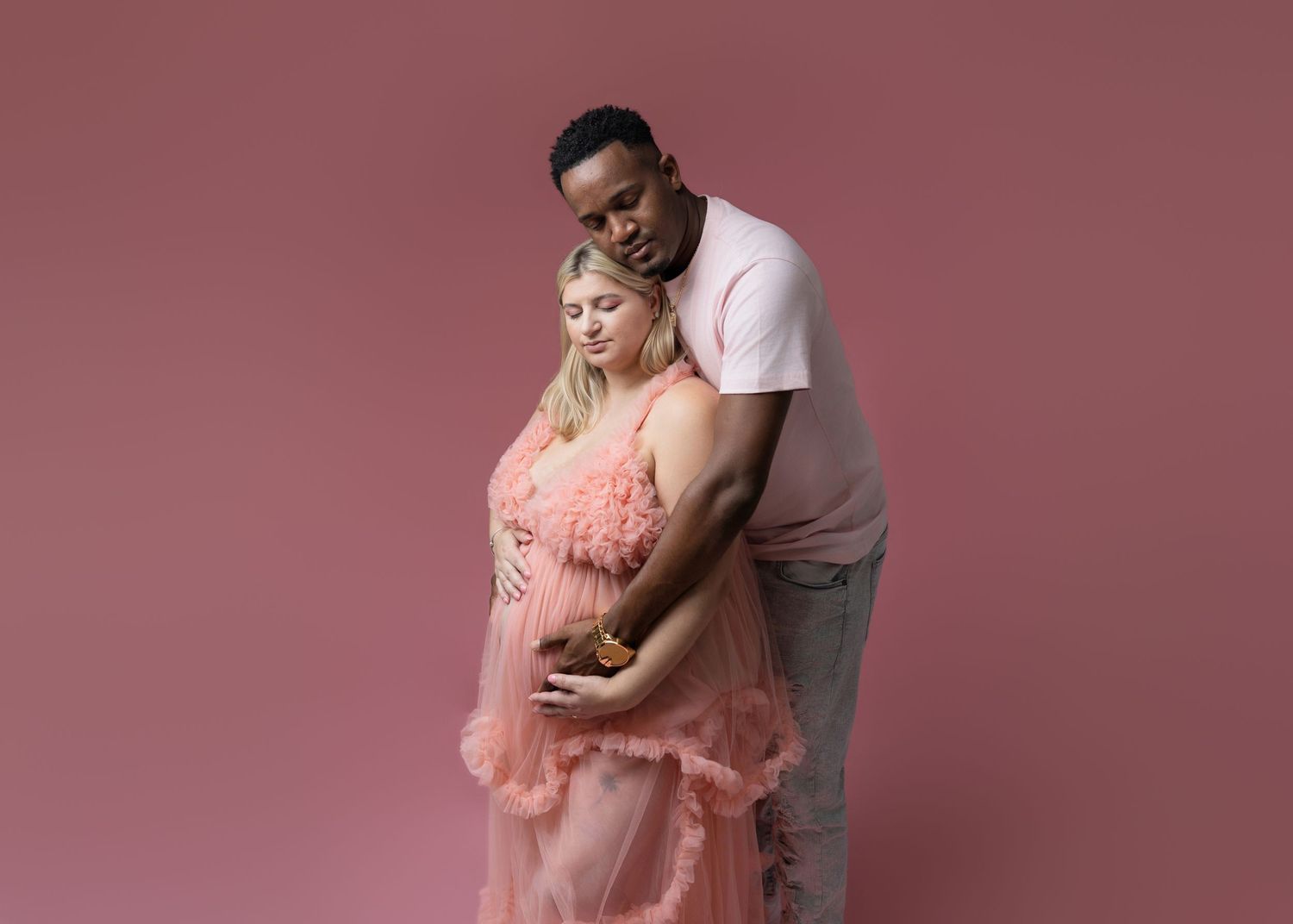 Couple embracing during maternity photoshoot wearing coral and neutral tones.