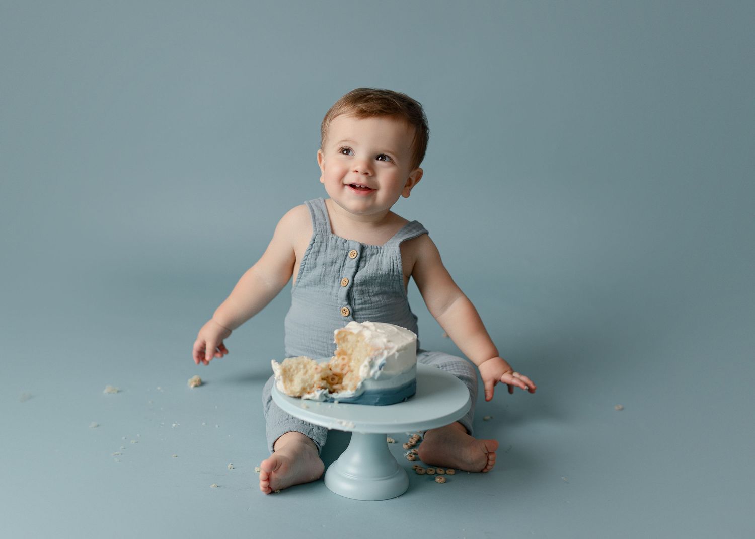 Baby in grey outfit plays with cake during first birthday smash cake photo session.