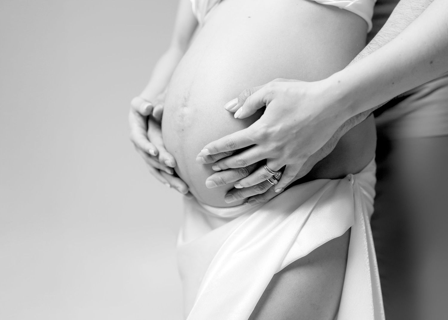 Close-up details of white fabric draping and hands creating elegant maternity photography composition.