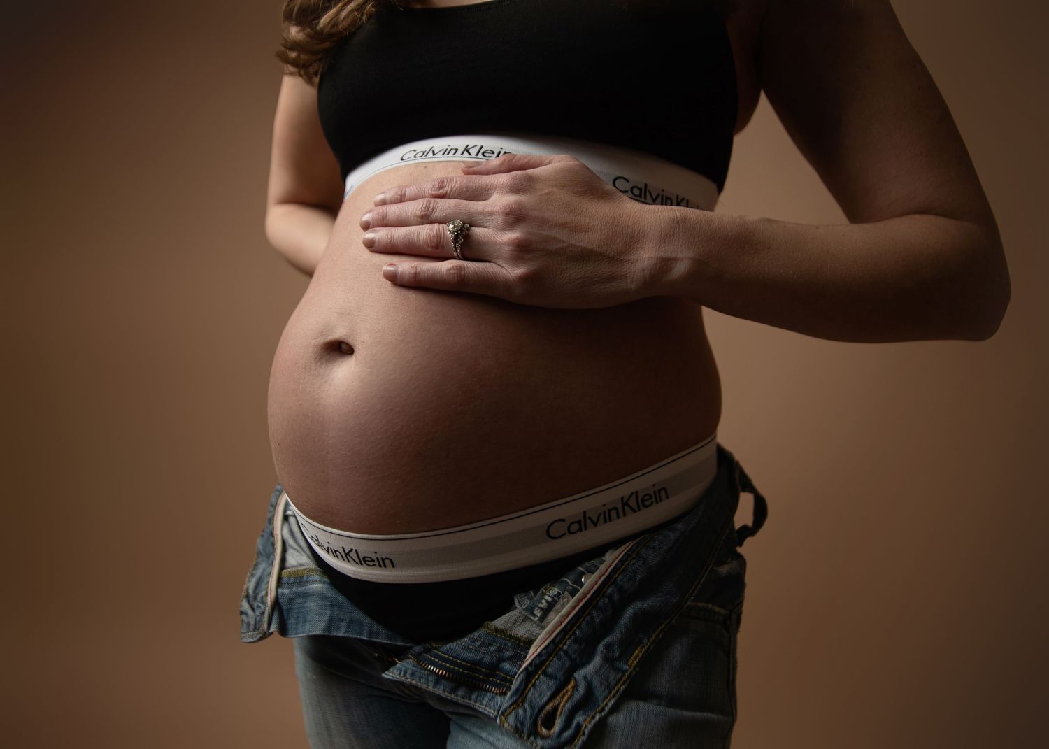 Close-up shots of pregnant belly with hands in casual maternity photography session.