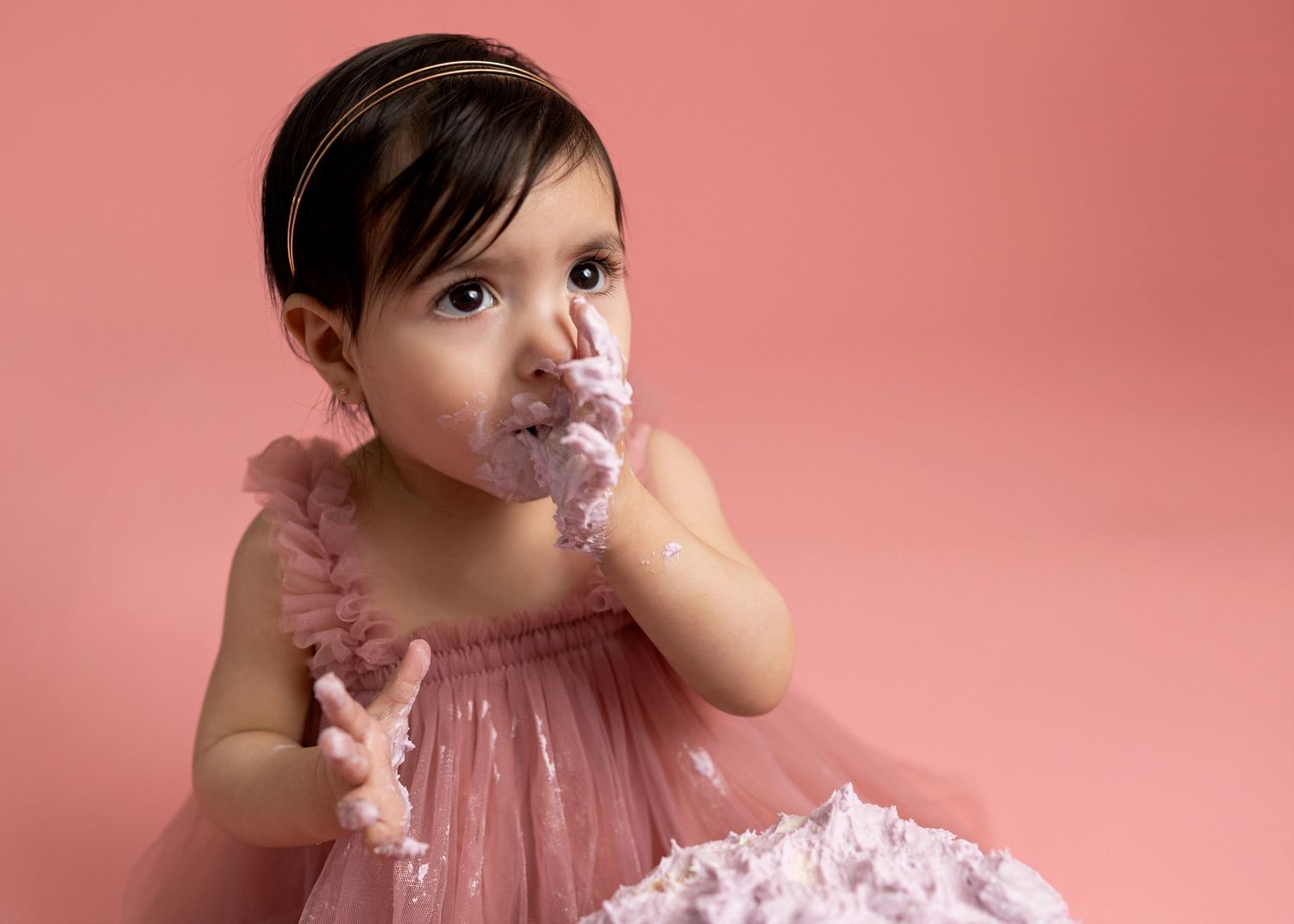 Baby in pink tulle dress crawls and plays during a photo session against a pink backdrop.