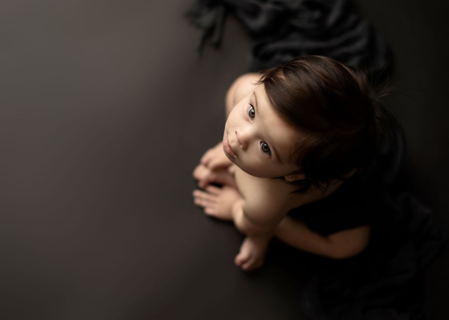 Artistic overhead portrait of smiling baby against dark background.