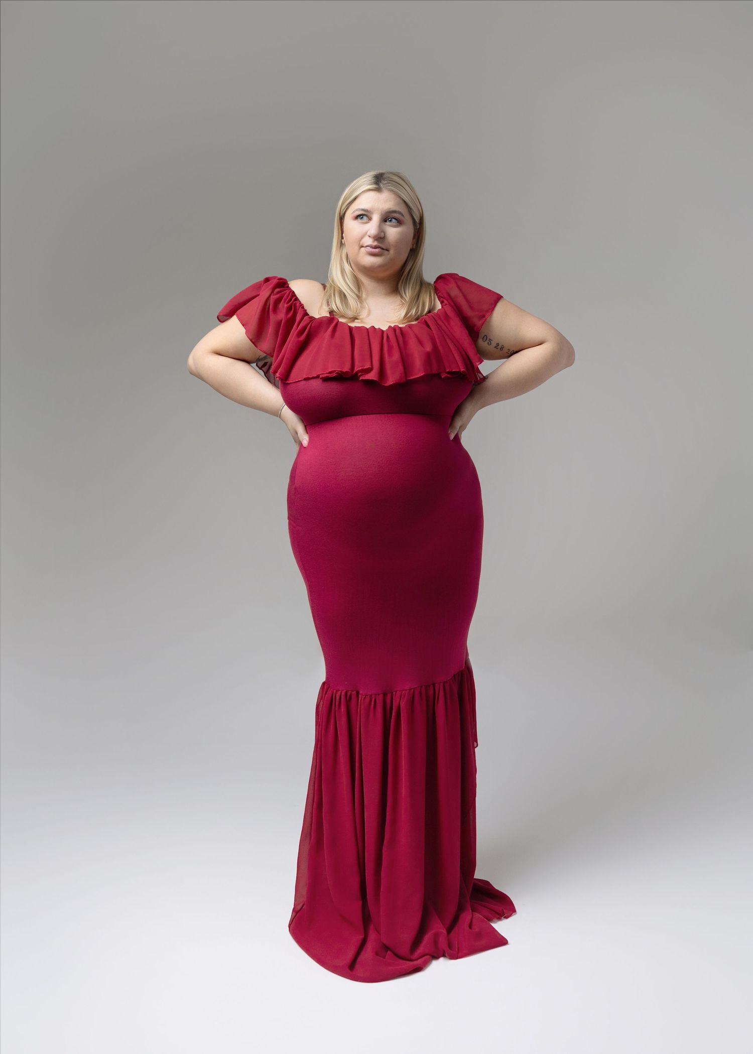 Woman in burgundy dress poses for maternity photos showing different angles.
