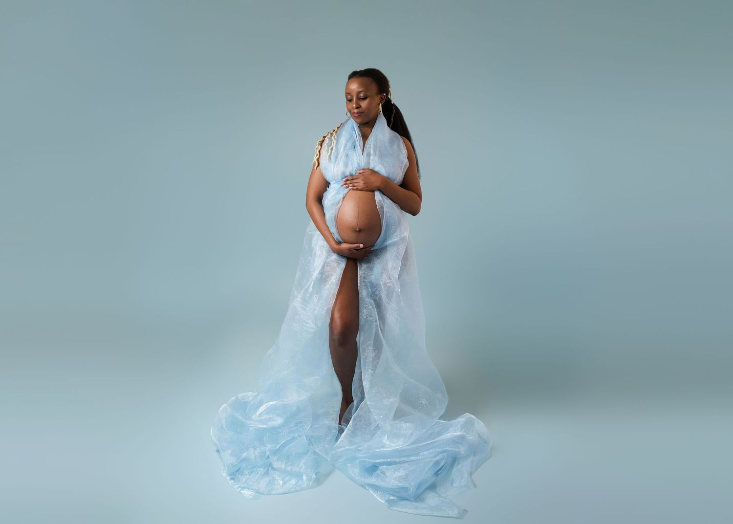 Ethereal maternity session with flowing light blue dress against blue background.