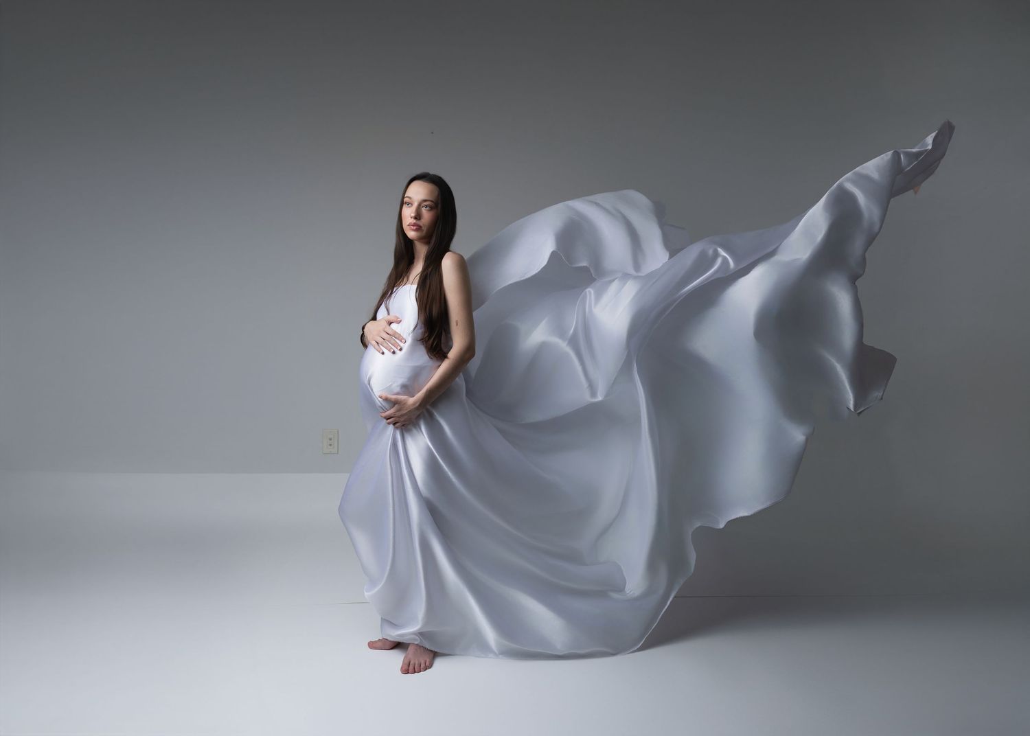 Ethereal white fabric billows and flows around a figure in a minimalist studio setting against a gray backdrop.