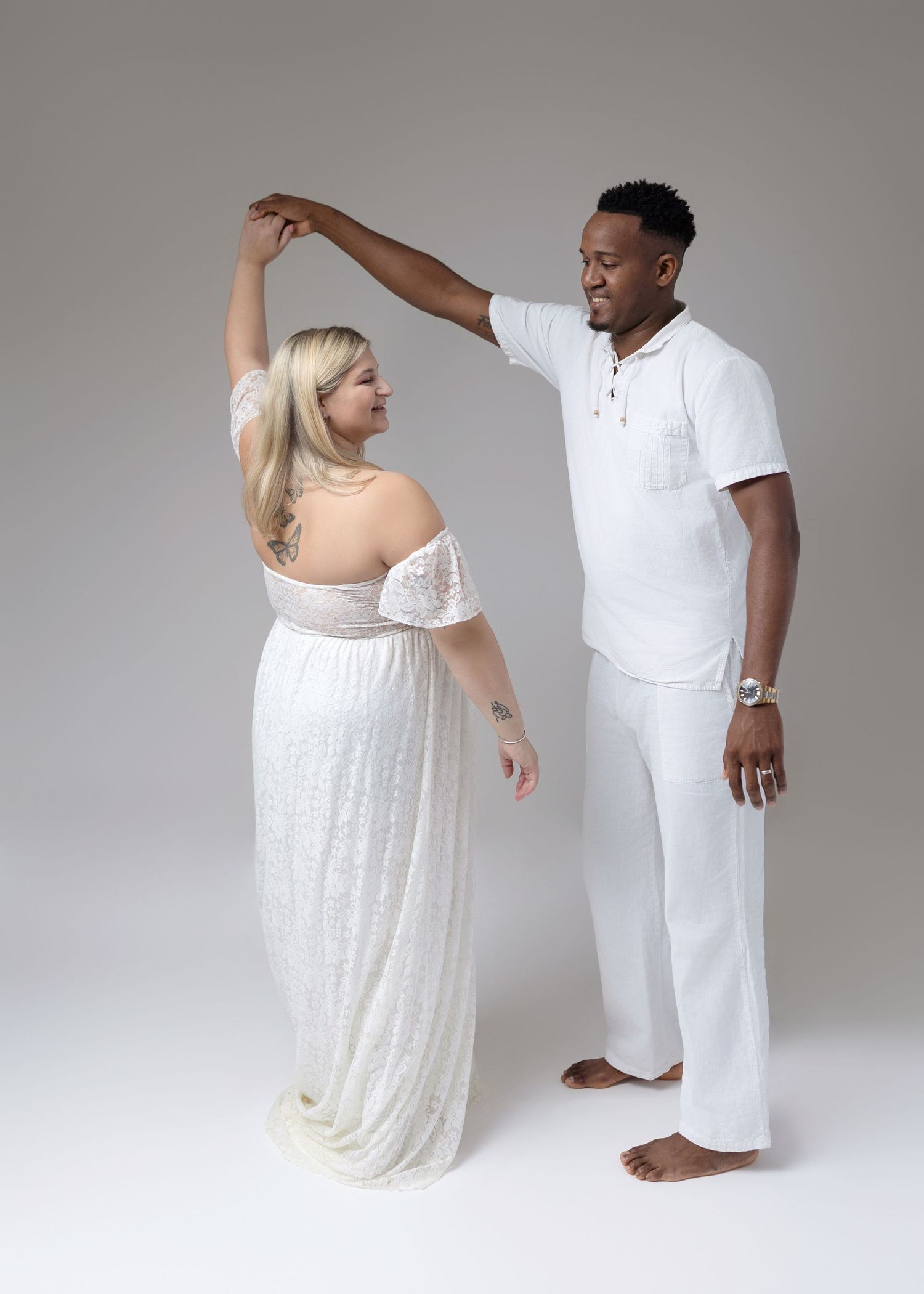 Couple in coordinating white outfits during studio maternity session.