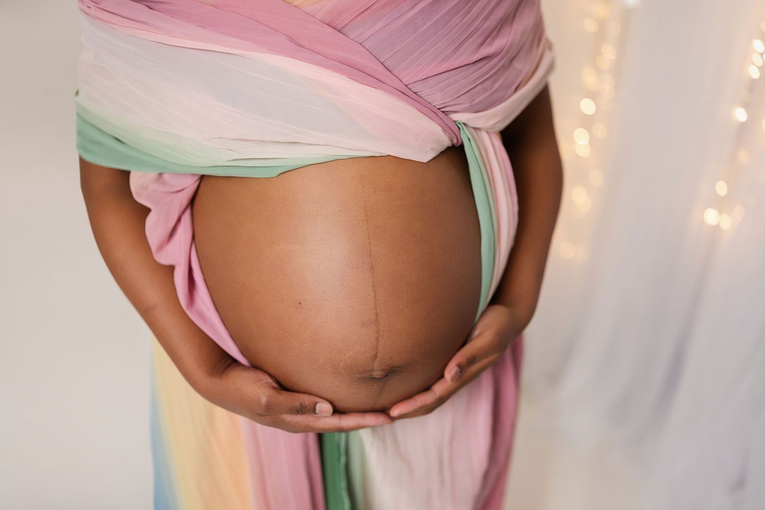 Maternity photography with soft pink and mint green draped fabric against white background.