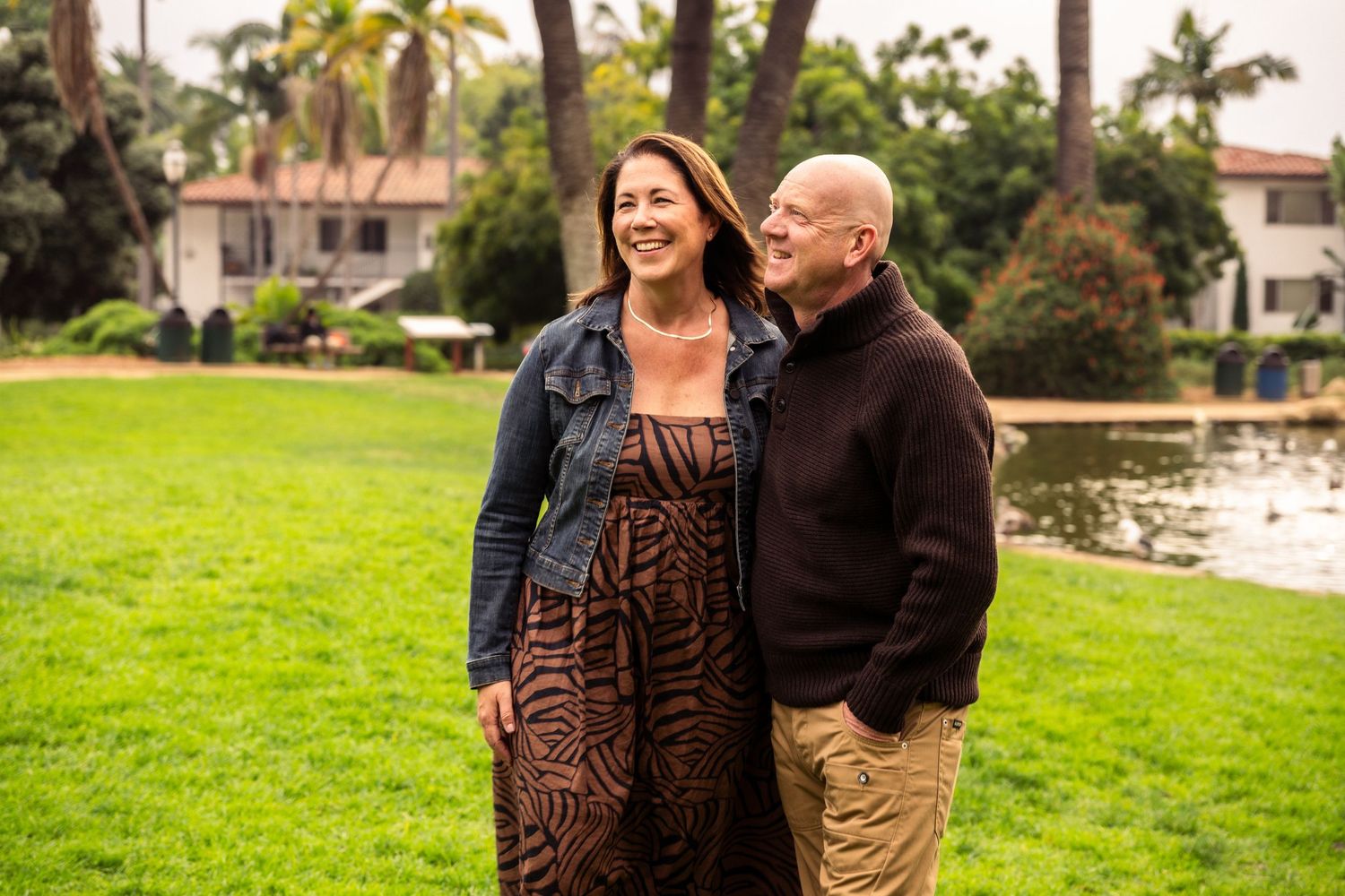 Editorial documentary couple photo of two adults standing together on a grassy area with palm trees, greenery, and soft natural light.